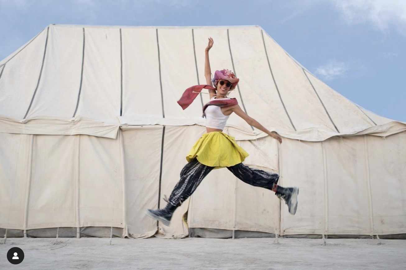  a lady jumping in front of a moroccan tent at burning man festival in the sahara desert 