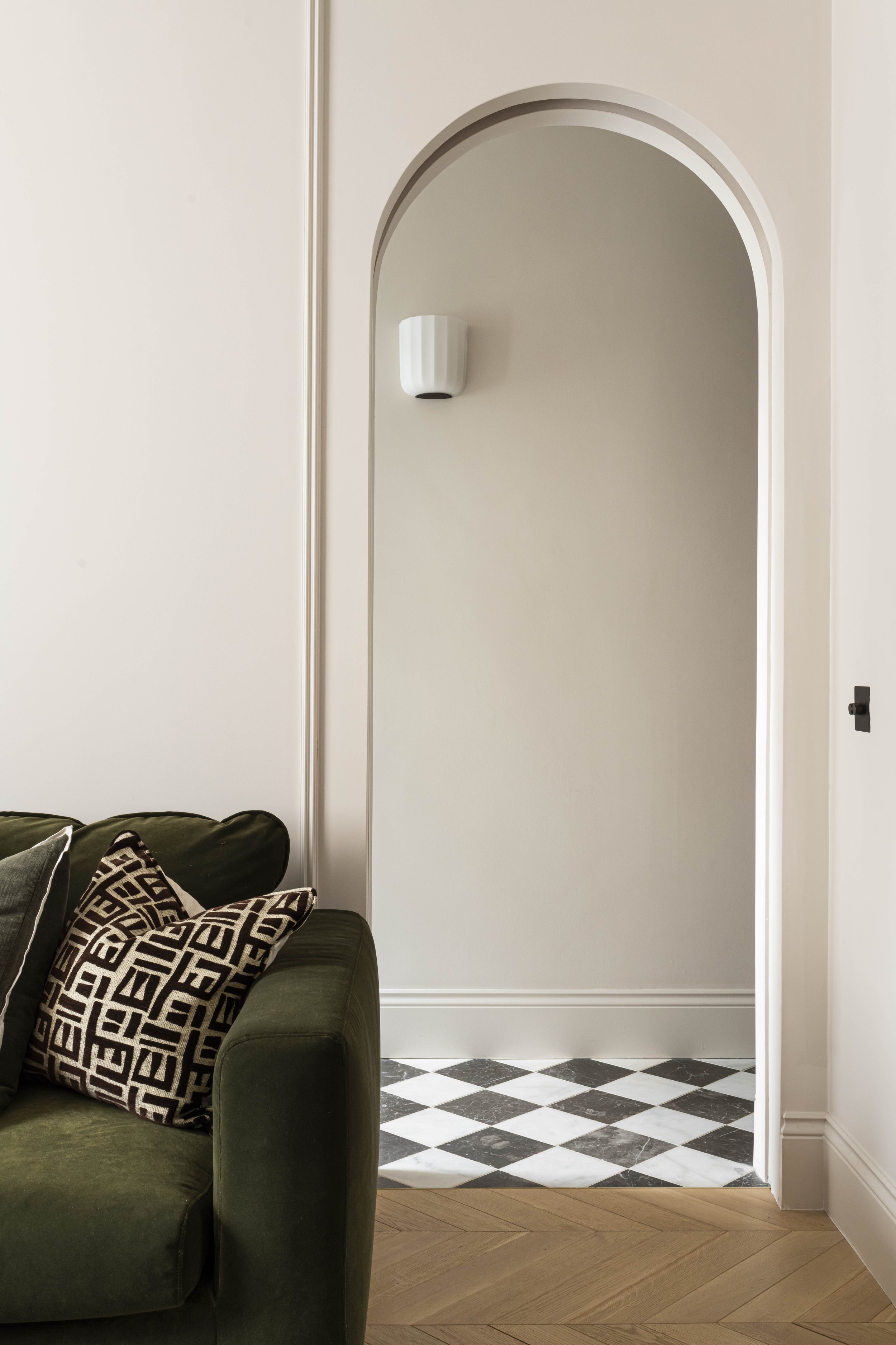 Arched pocket door, olive green sofa, marble chequerboard tiles and neutral wall colour in a Victorian house refurbishment by Studio Zeal