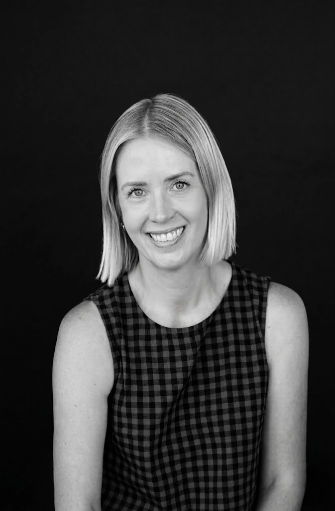 Black and white portrait of Amanda Kelly of Studio Zeal with shoulder-length blonde hair, wearing a checkered sleeveless top, against a dark background.