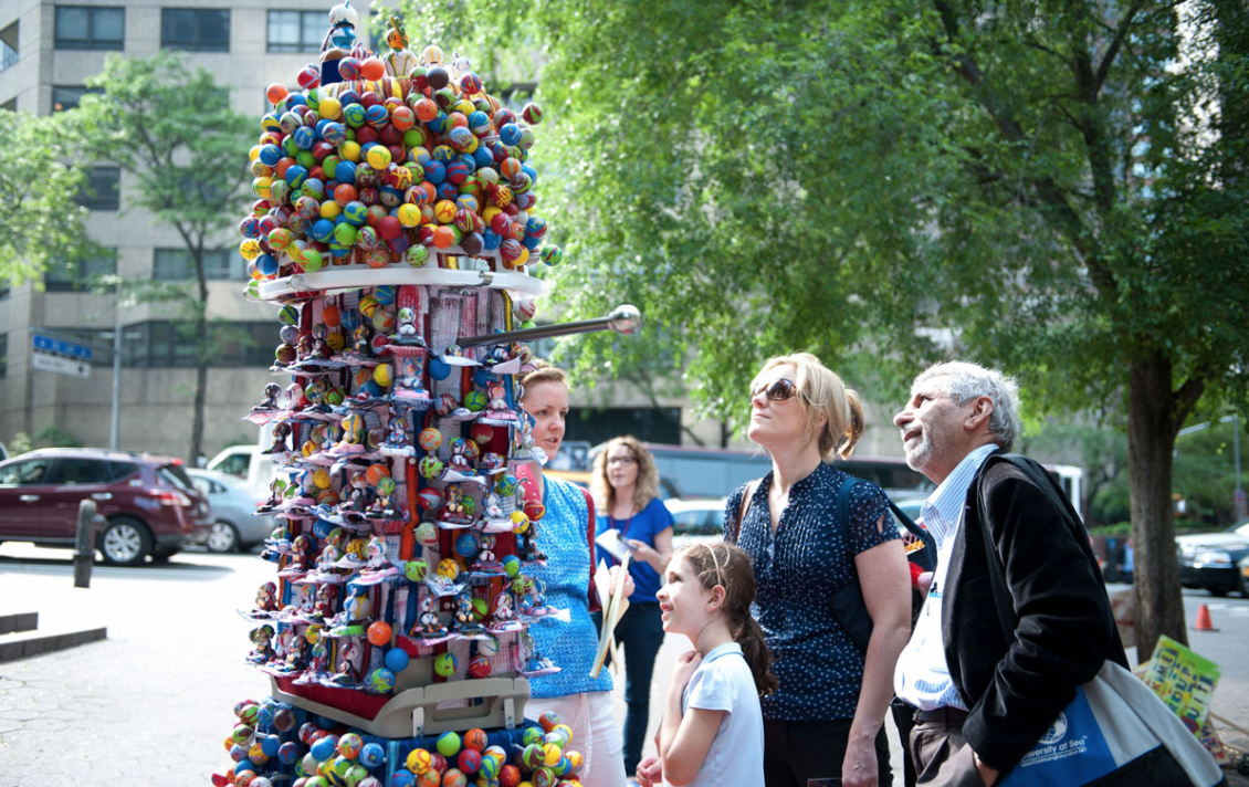 Group Suit: A Day in the Park, May 23, 2012, presented by NYC Parks & Recreation, Dag Hammarskjold Plaza, across from the United Nations Headquarters, New York, NY Manning creates an interactive sculpture out of thousands of ping-pong balls with hand-painted faces, altered solar power bobble head dolls, plastic bins, containers, fabric and other mixed media. The laundry basket head of the sculpture is removable and audience members are invited to try it on and become immersed in hundreds of faces and novelty items. The face of each participant becomes nicely framed within the basket and a photographed portrait is offered to each person who wears it. Manning’s goal is to encourage people to distinguish themselves from the crowd and to feel a stronger sense of self-identity. 