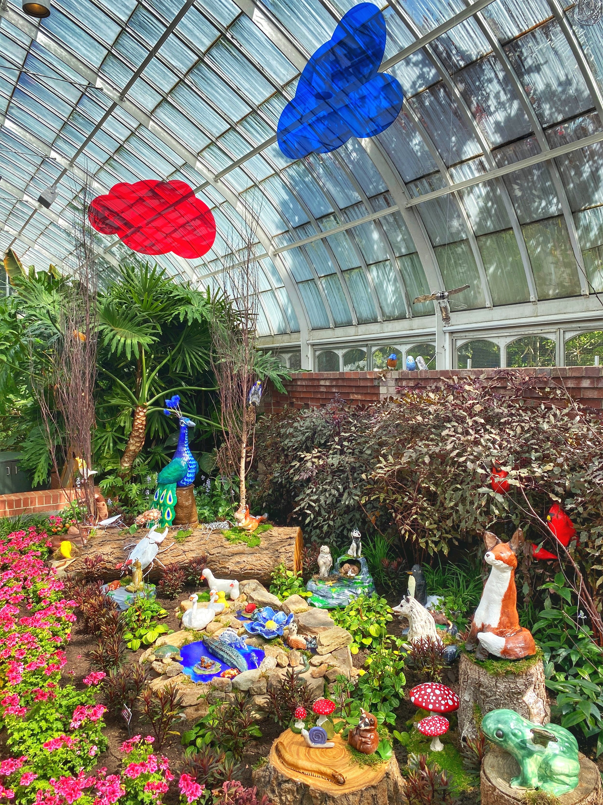 Red and blue clouds above a menagerie of ceramic animals in a glass conservatory at the Phipps