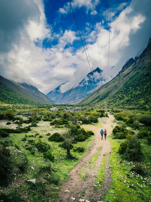Two hikers walk a dirt path under telephone wires on the Manaslu Circuit trek in Nepal