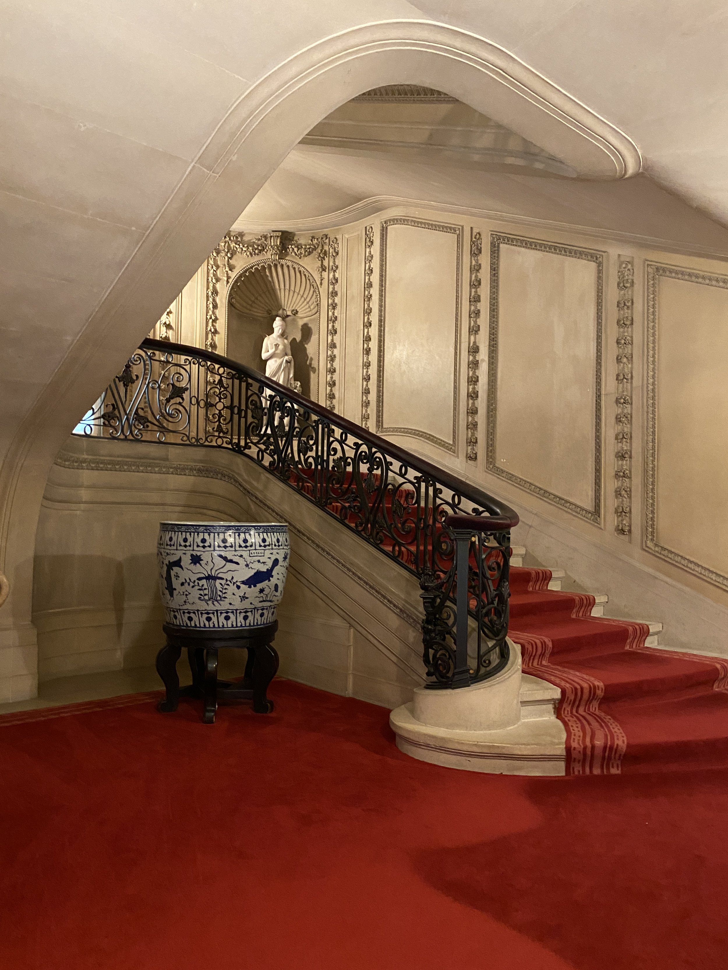 The grand staircase, with statues, large urn and red carpet at the Vanderbilt Mansion