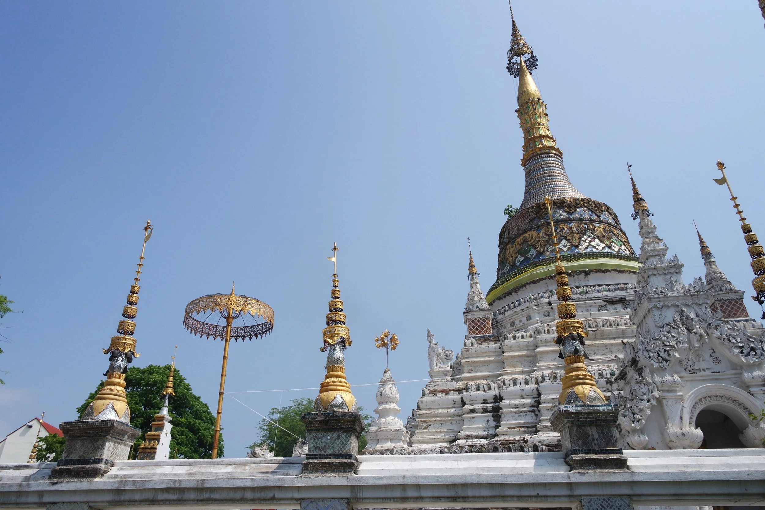 The beautiful whitewashed chedi at Wat Saen Fang is surrounded by gold umbrellas and offeratory fires