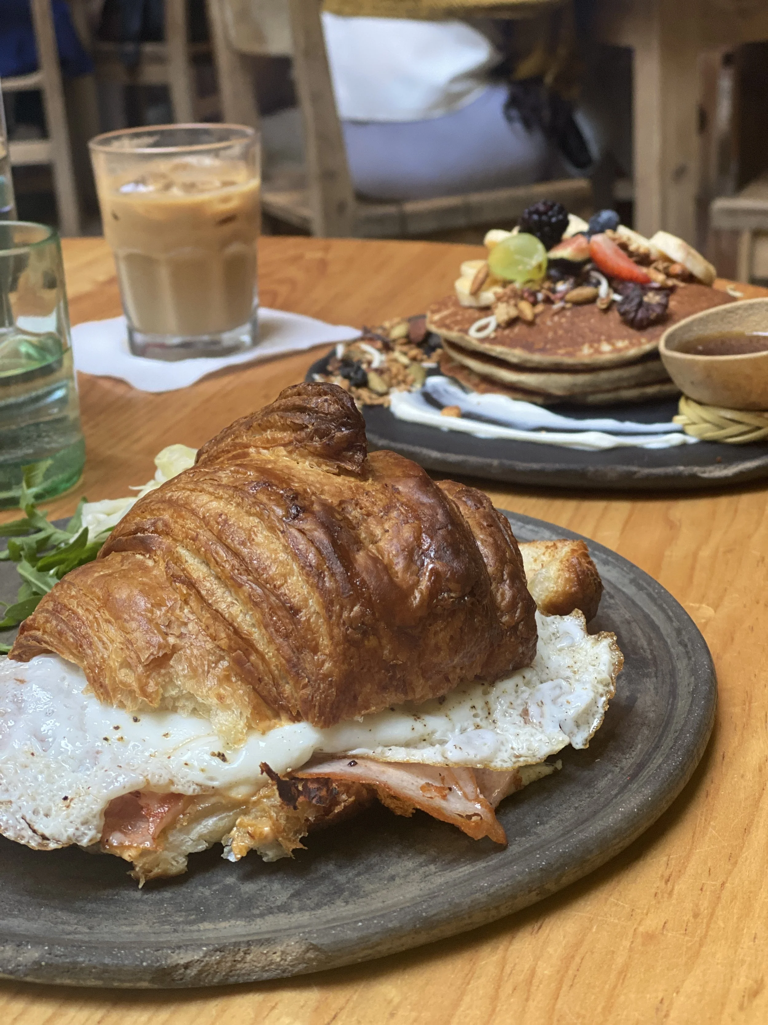 Croissant sandwich with turkey and egg, pancakes topped with fruit and iced coffee on table at Boulenc cafe in Oaxaca