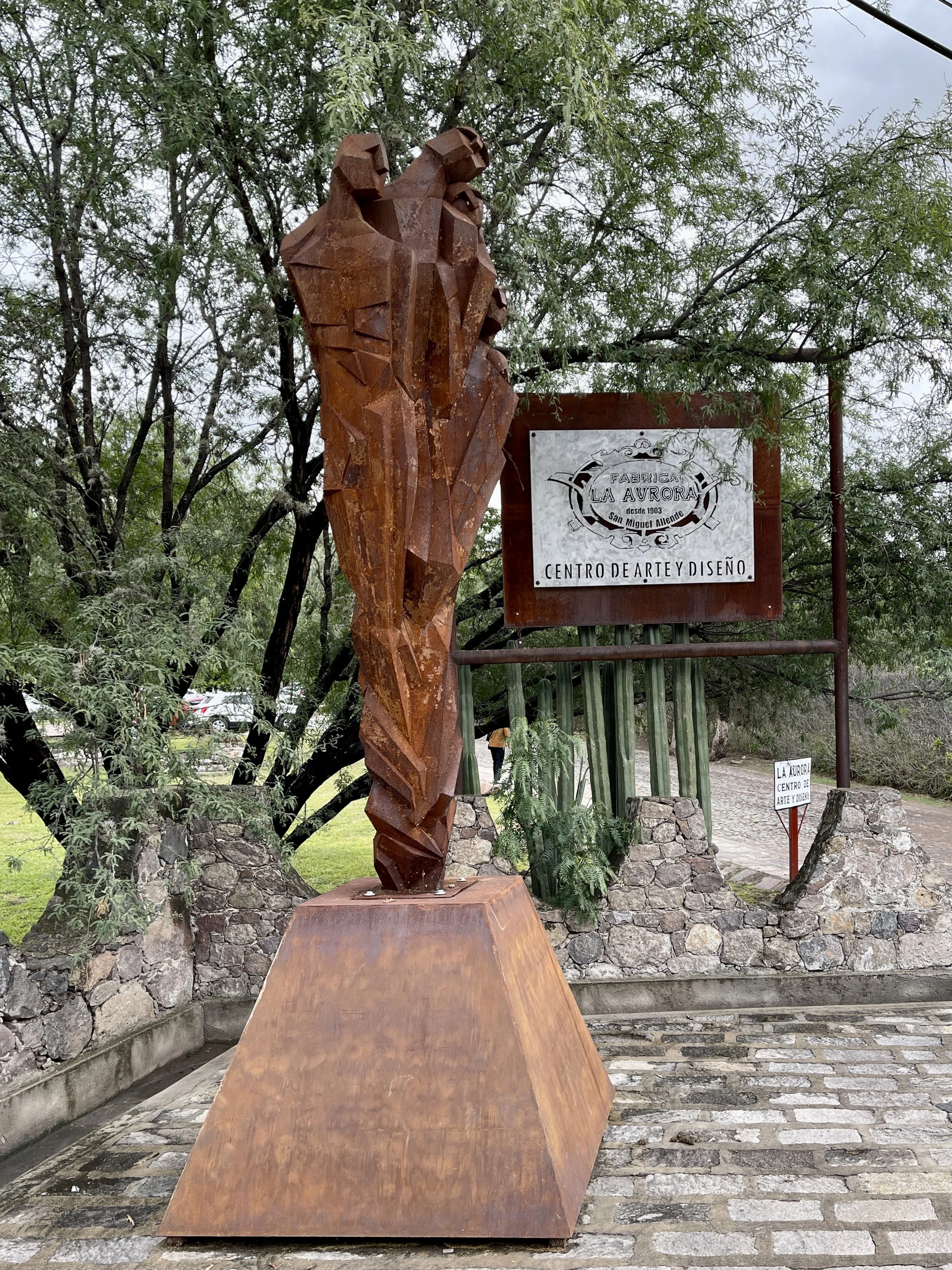 Angular metal statue of people in a cluster by the sign for Fabrica La Aurora