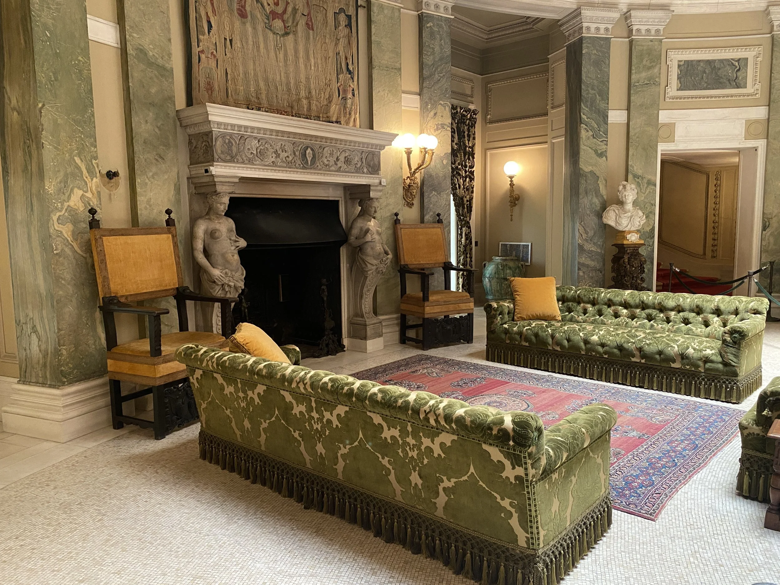 The reception room at the Vanderbilt Mansion, with green sofas, Oriental rug and fireplace with Classical sculptures