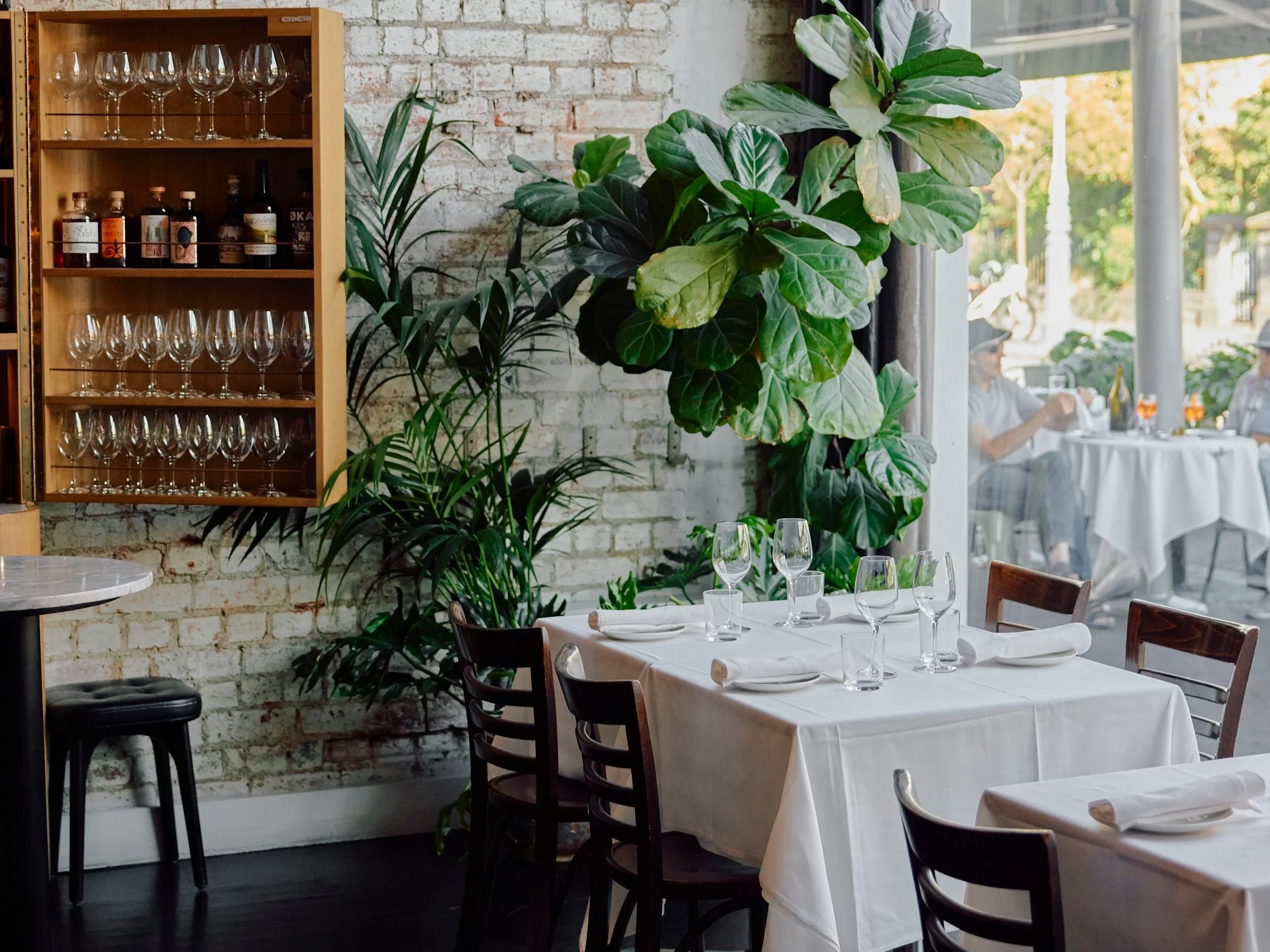 A white tablecloth-covered table  near a cupboard with win glasses at Cutler in Melbourne, Australia