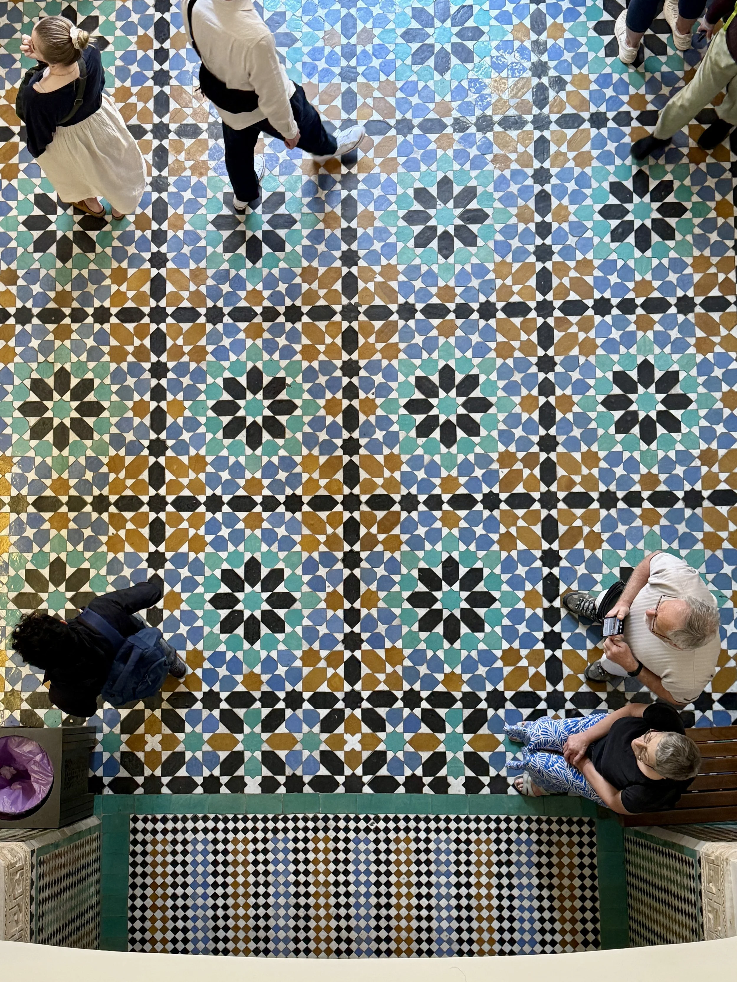 People  walk on the zellij tiled floor in the lobby of Ben Youssef Madrasa