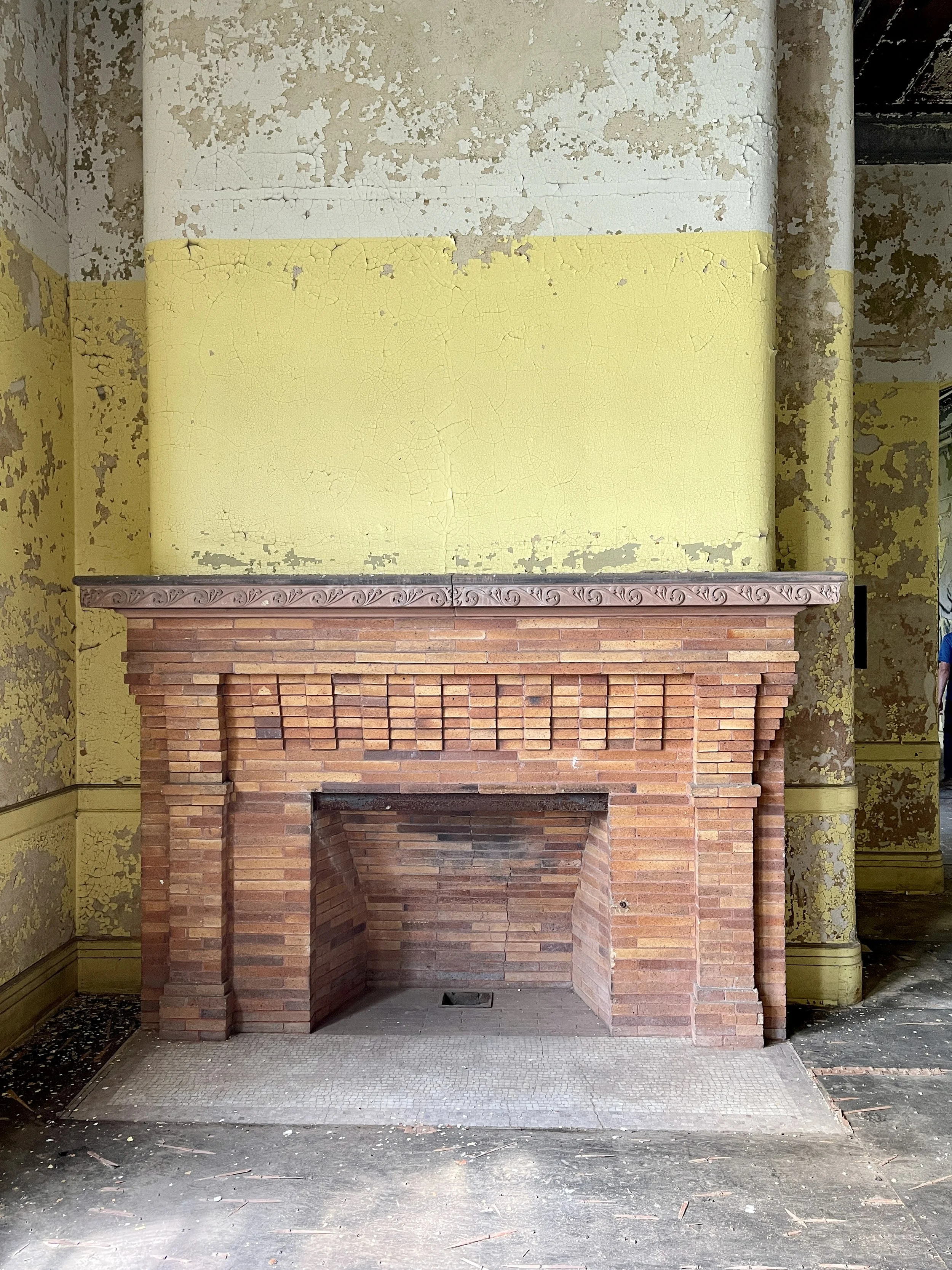 Brick fireplace by peeling yellow walls in women's ward at the abandoned Buffalo State Asylum
