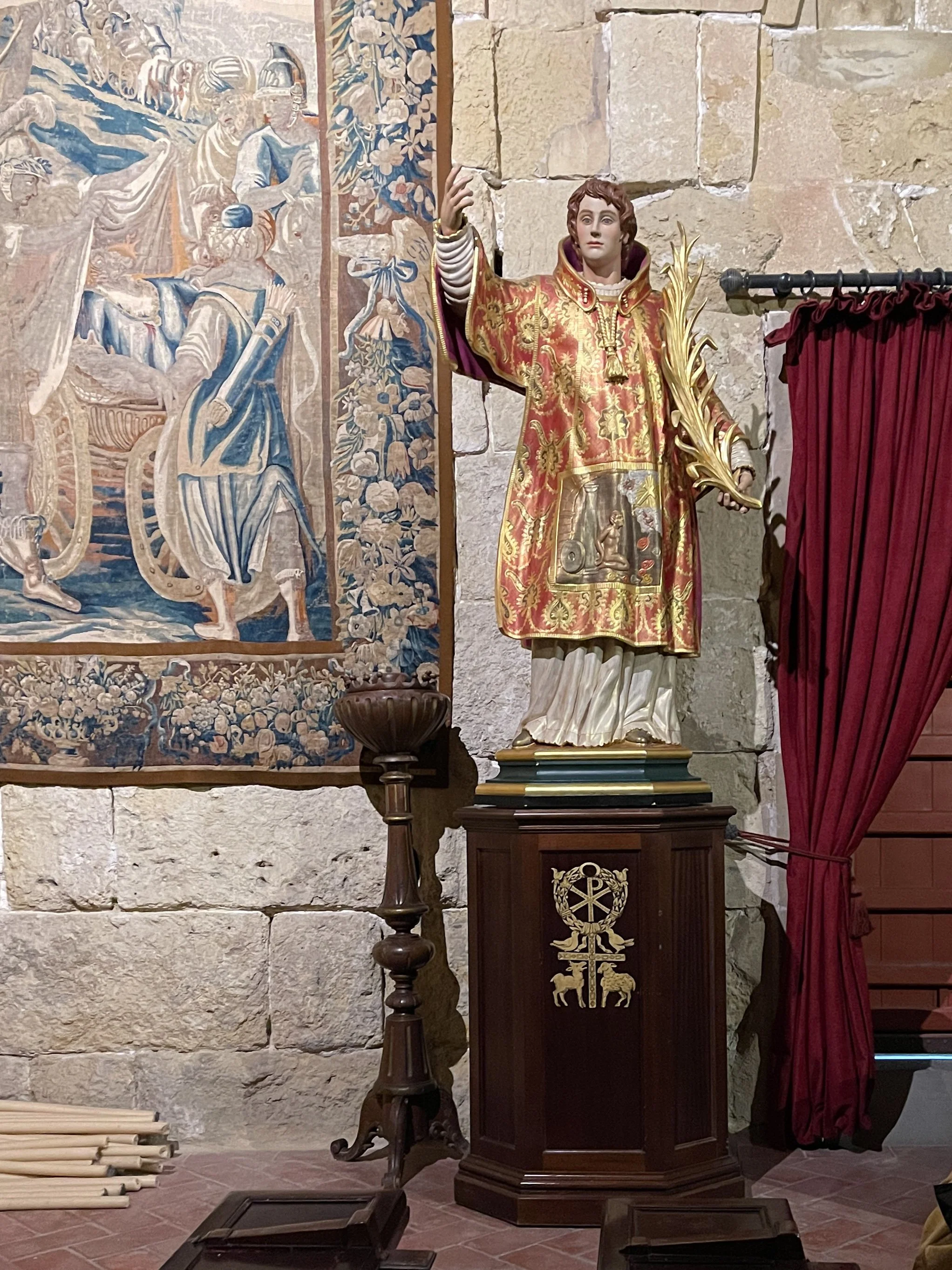 Statue of male saint with arm raised next to tapestry in the Mezquita in Córdoba, Spain