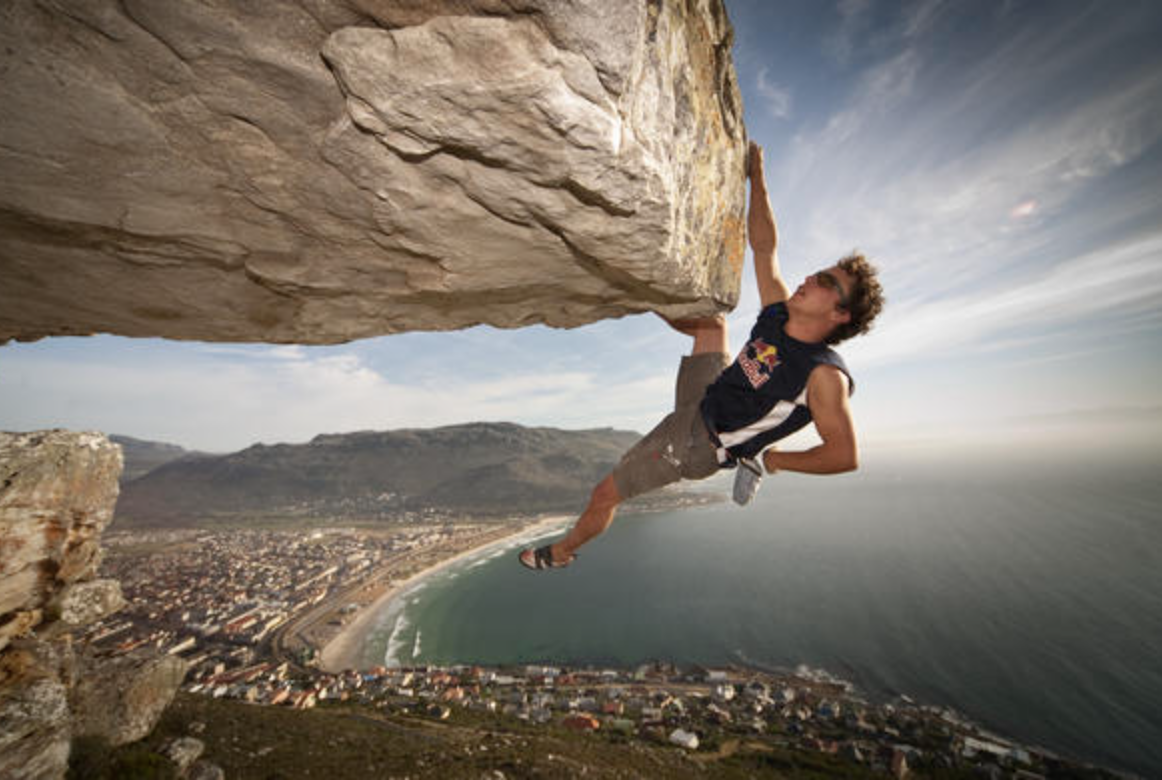 A mab climbs a rock ledge on Table Mountain high avove Cape Town, South Africa