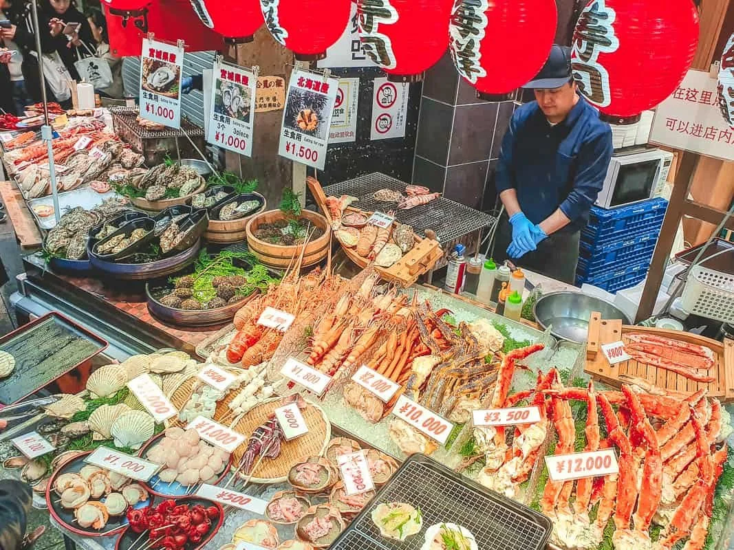 A seafood vendor at Kuromon Market in Osaka, with crab legs and other items for sale under paper lanterns