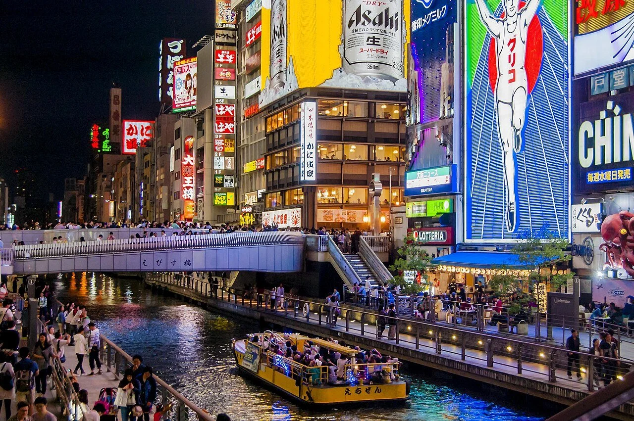 A tour boat glides under the neon-lit canal and Ebisu Bridge in Dotonbori in Osaka, Japan