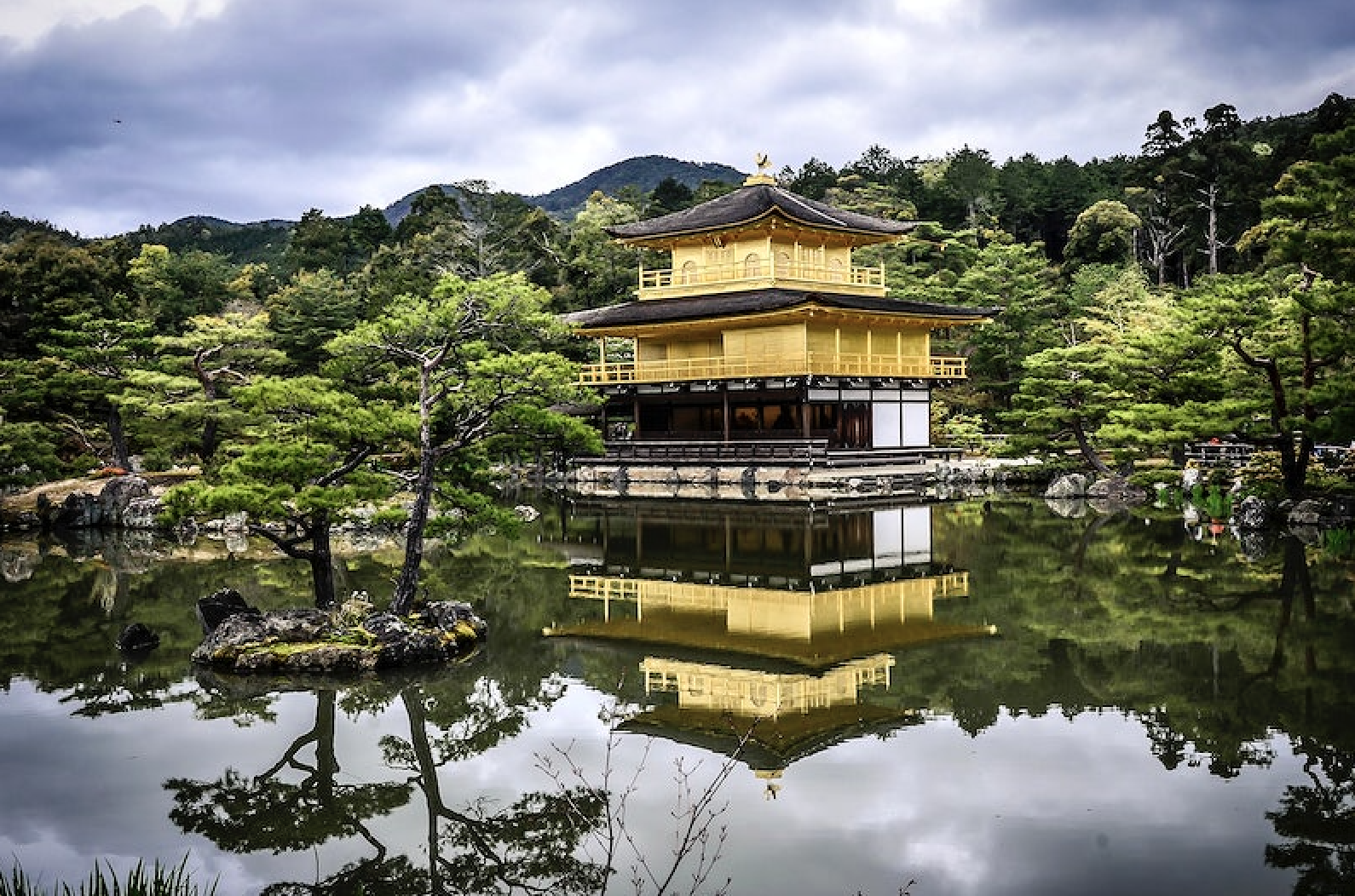 The Golden Pavilion in Kyoto, Japan, with yellow tiers among trees reflected in the water