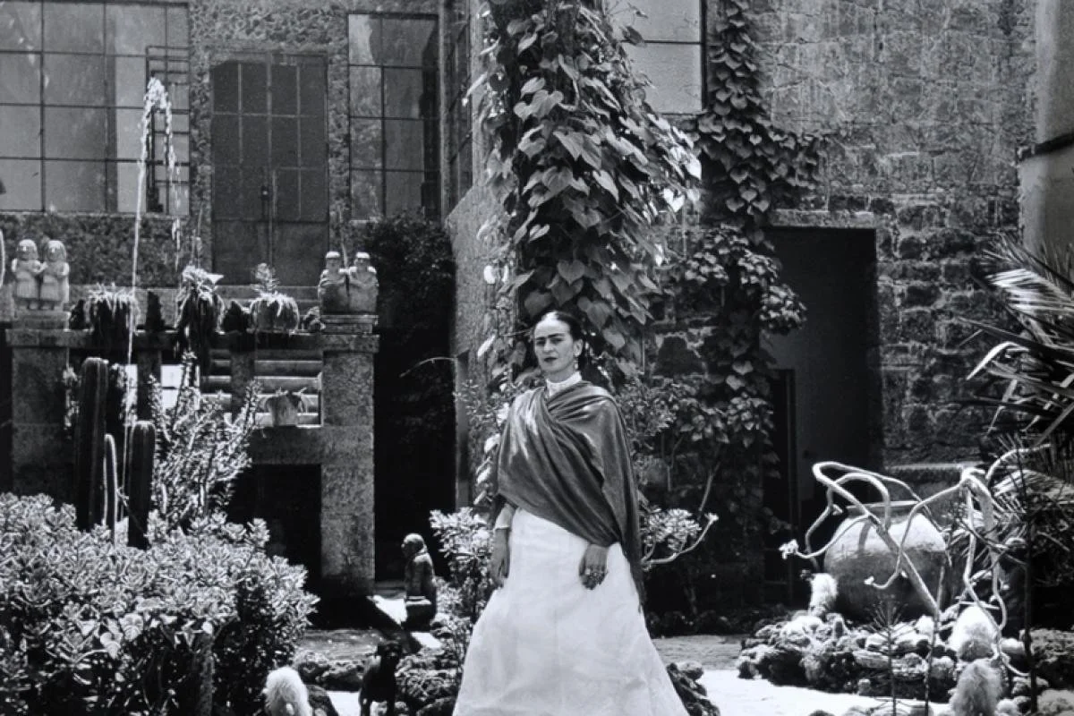 Frida Khalo, wearing shawl and white dress, standing in the garden of her home and studio, the Casa Azul