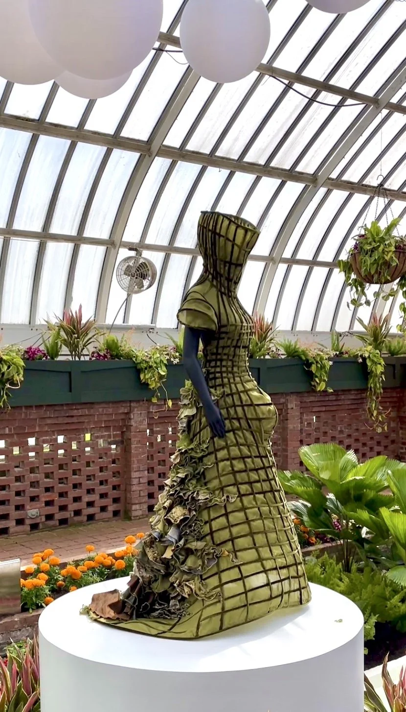 Mannequin wearing olive green dress with brown lattice work and hood in Sunken Garden at the Phipps Conservatory
