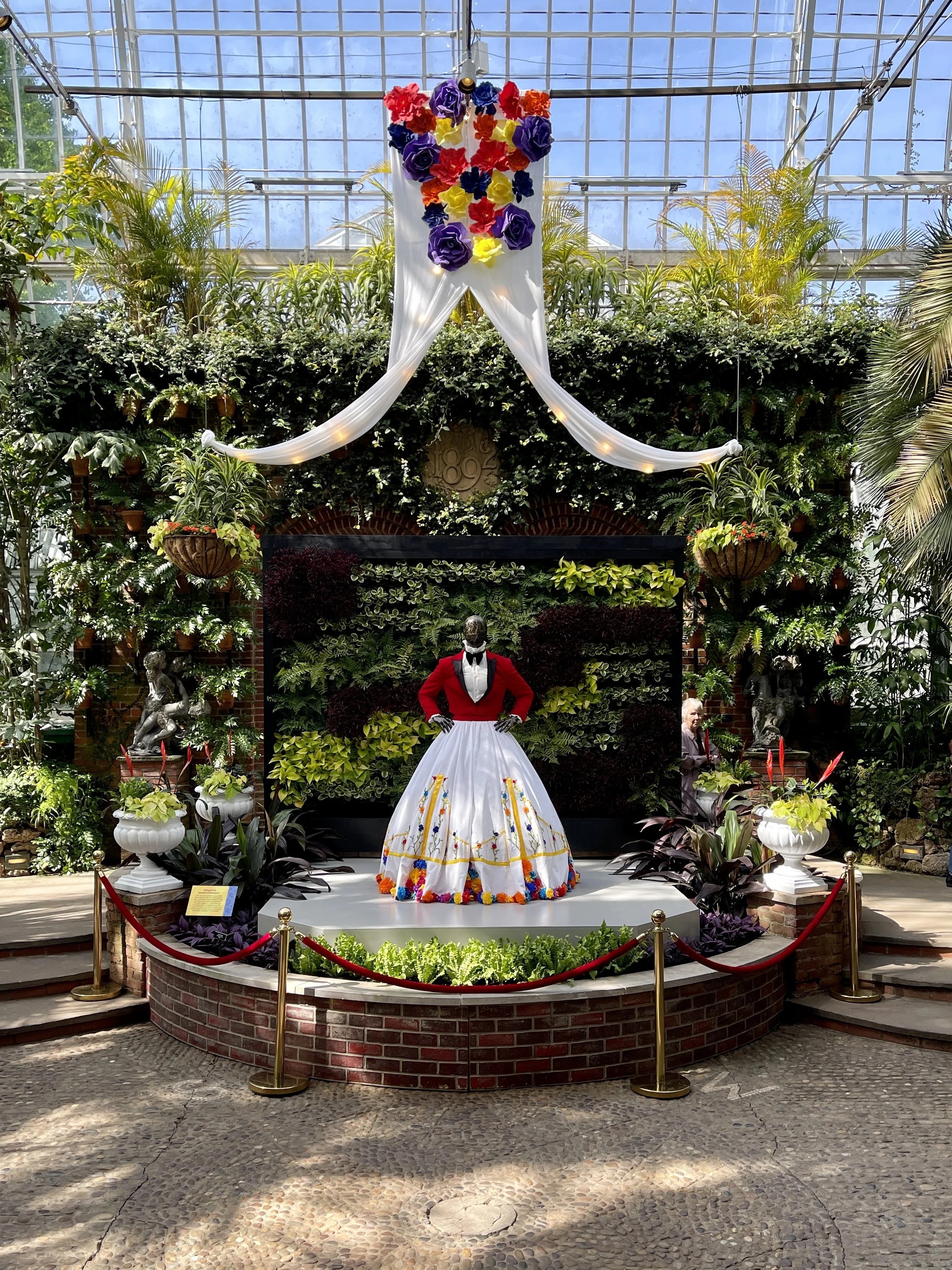 Mannequin with red velvet jacket and Mexican-inspired skirt in large conservatory filled with plants at the Phipps