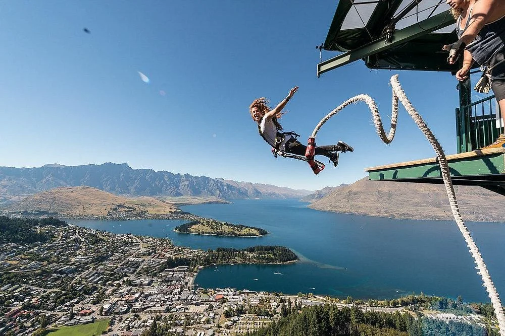 A person bungee jumps off a platform by the water over Queenstown, Australia