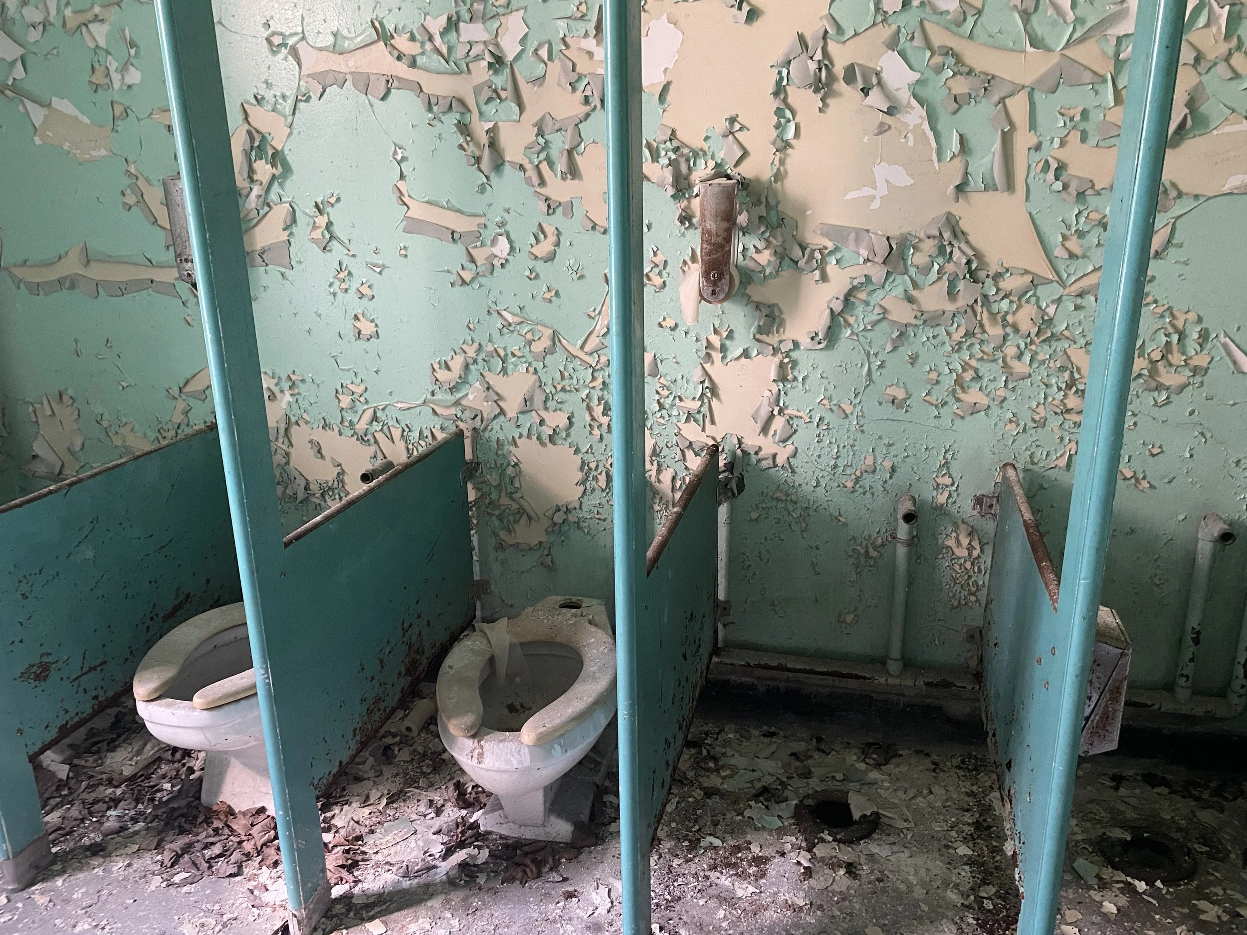 Bathroom with old toilets, aqua stalls, peeling paint in the abandoned Buffalo State Asylum