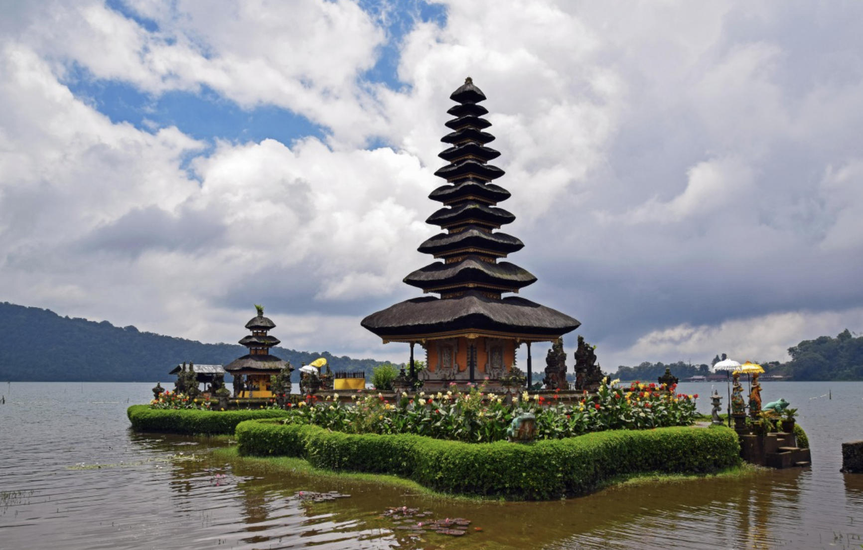 Multi-tiered Balinese temple on small island with flowers and hedges
