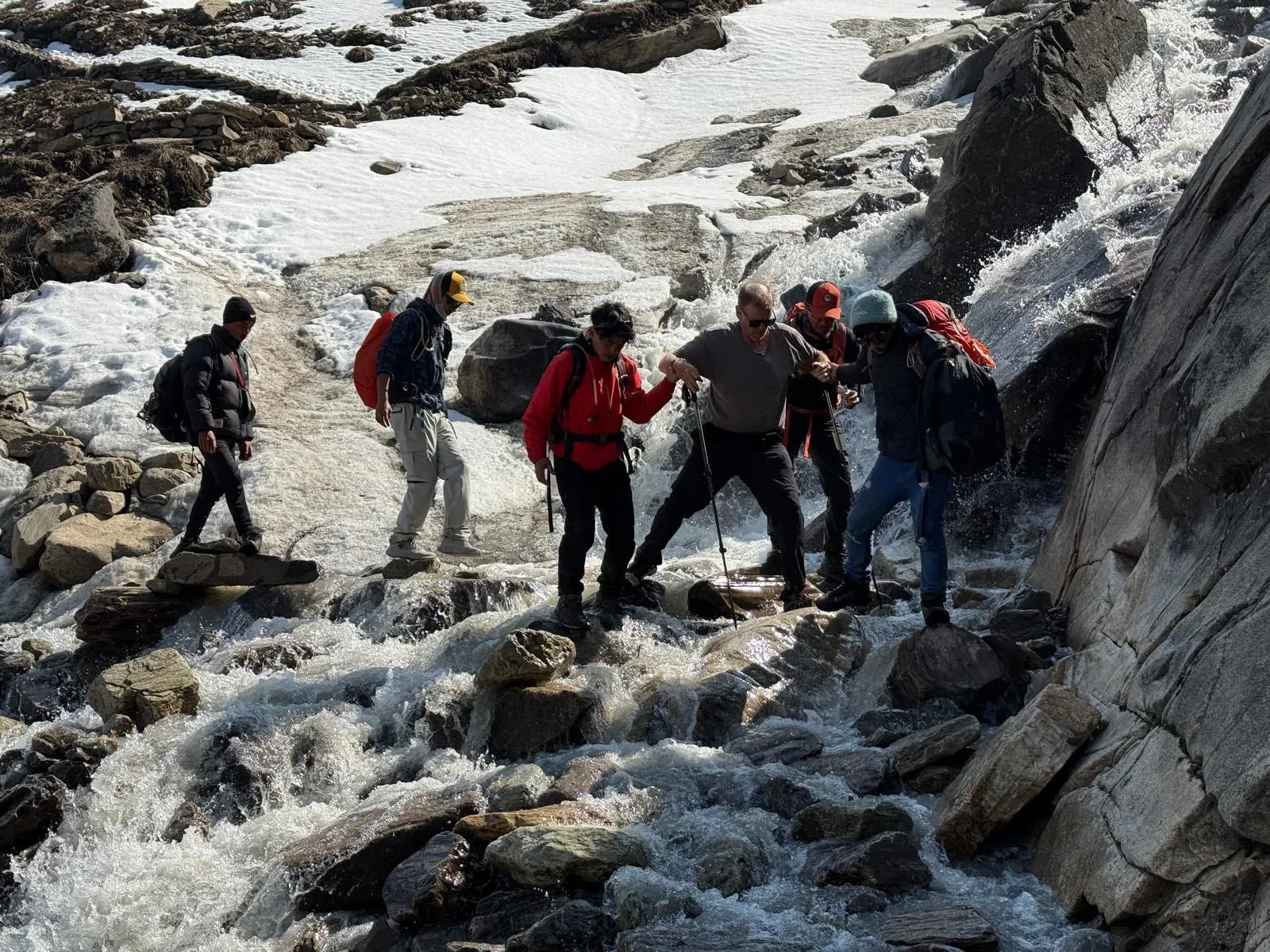 Trekkers help a man cross a river on rocks along the Manaslu Circuit trek in Nepal