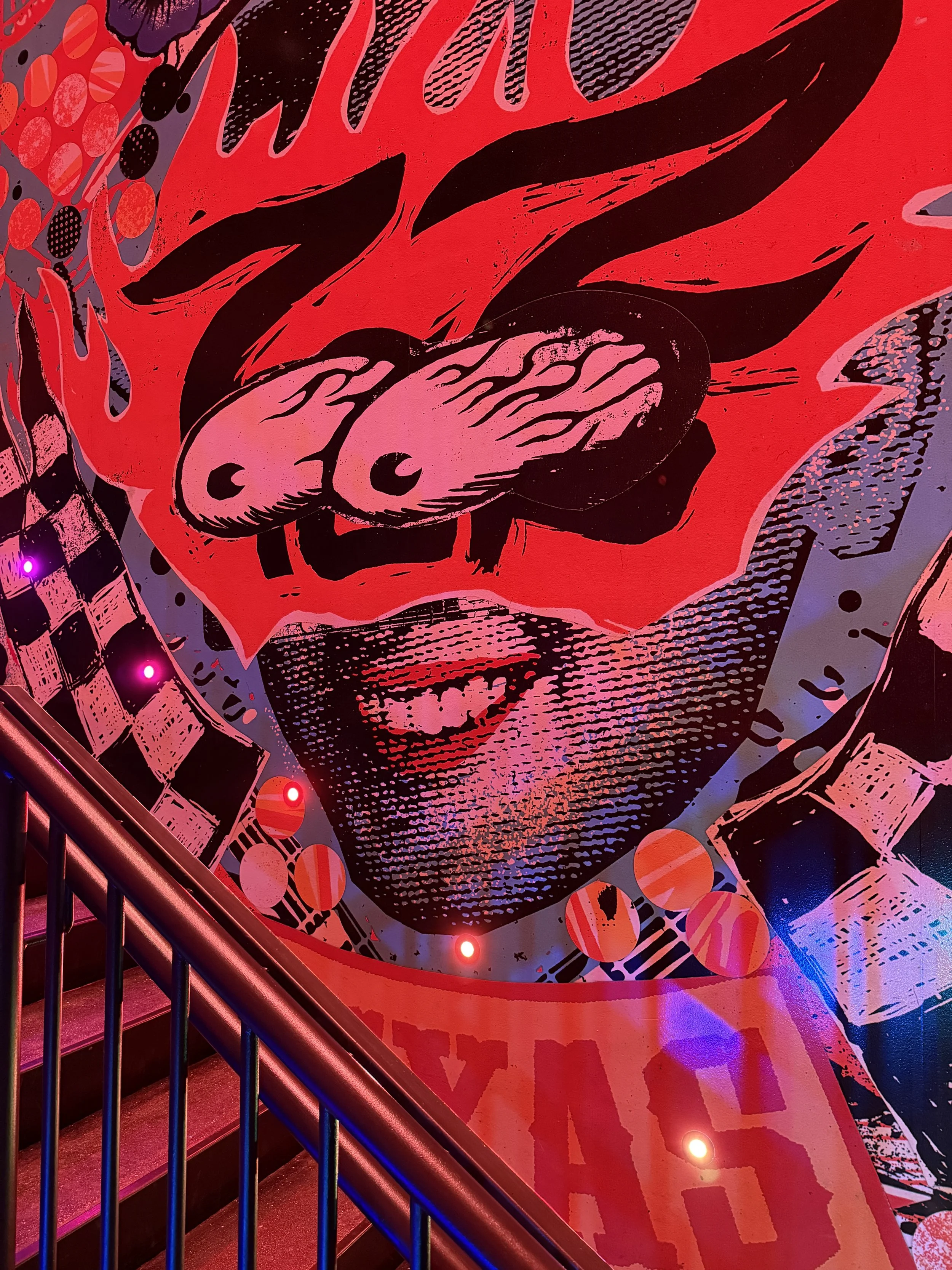 Red collage artwork of bulging eyes by a staircase at Meow Wolf Radio Tave in Houston, Texas