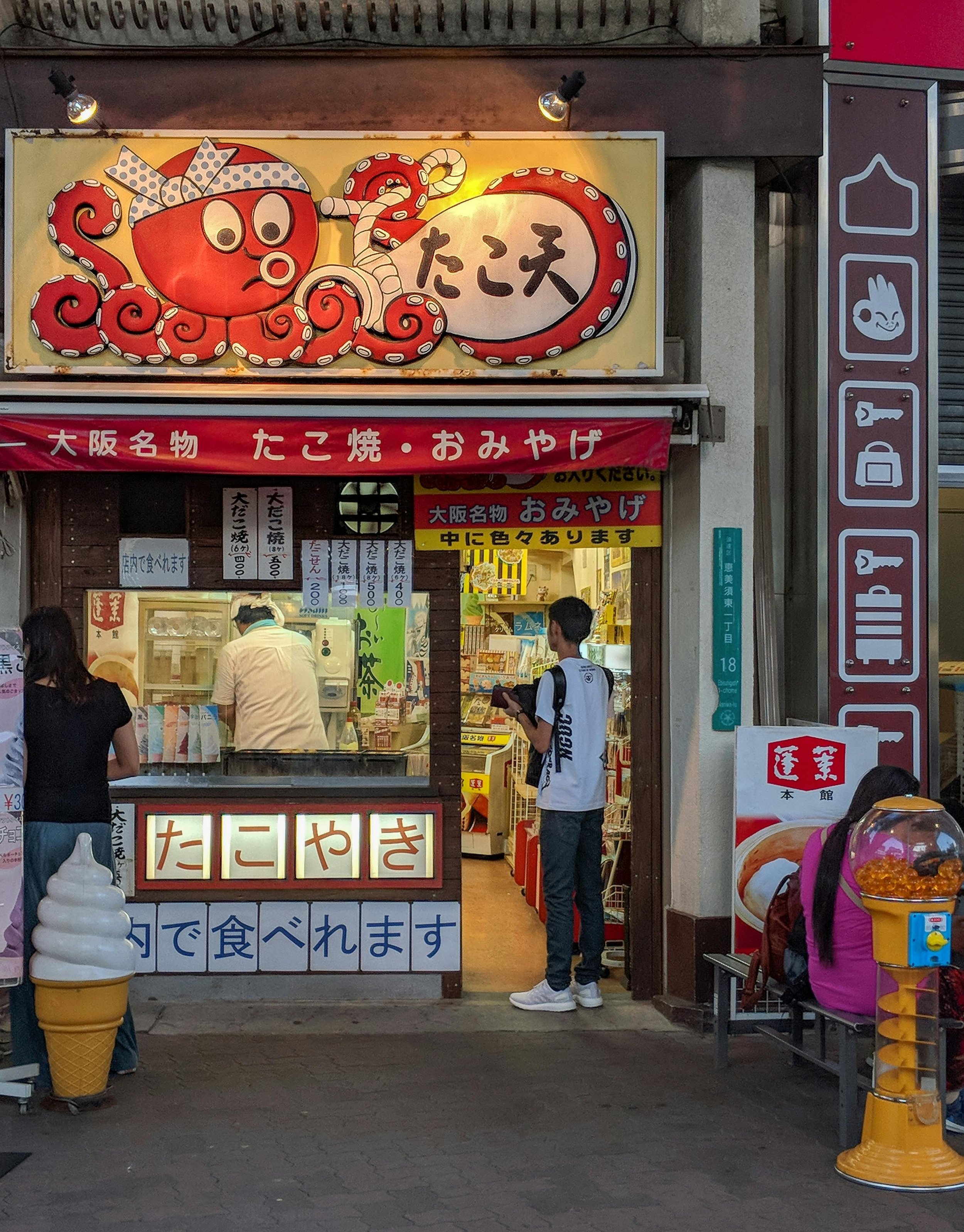 A boy stands in the doorway of a takoyaki restaurant with an octopus sign in Osaka, Japan