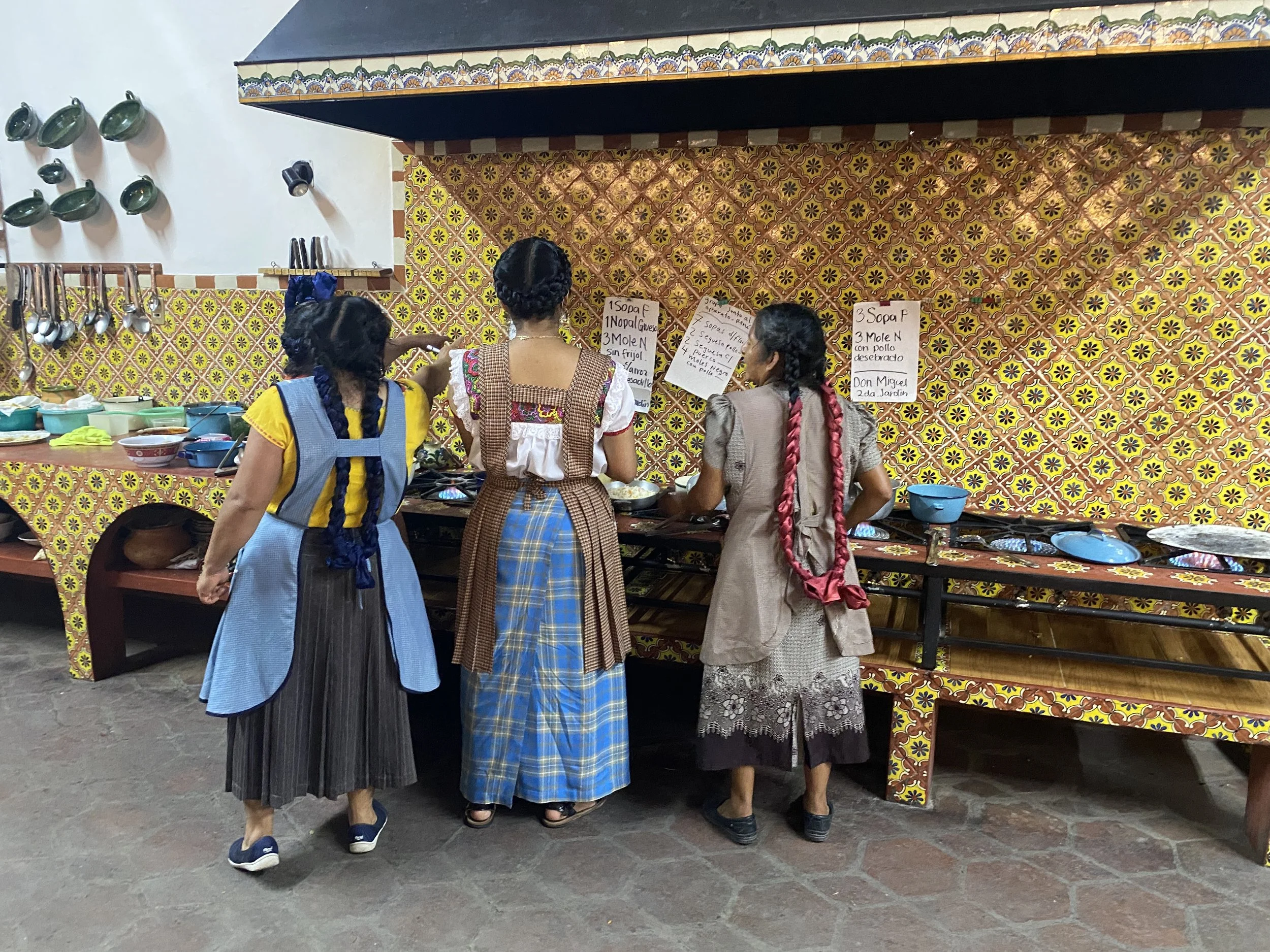 Three cooks seen from behind in yellow tiled open kitchen at Tlamanalli restaurant in Oaxaca, Mexico