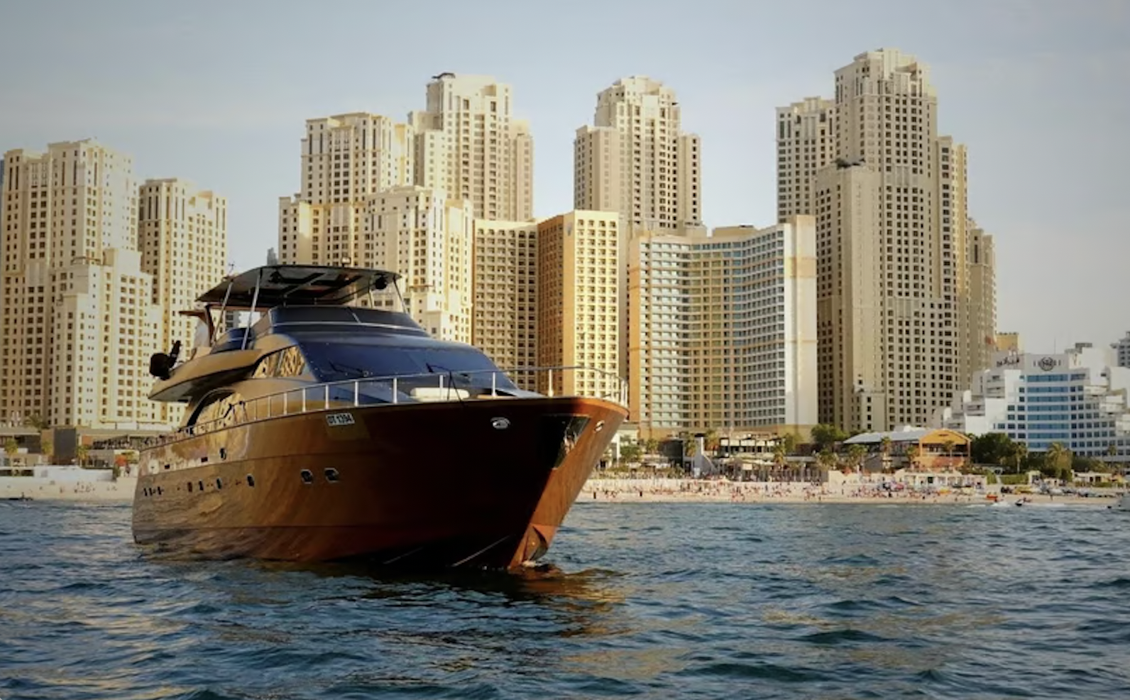 A yacht off of a beach and skyscrapers in Dubai