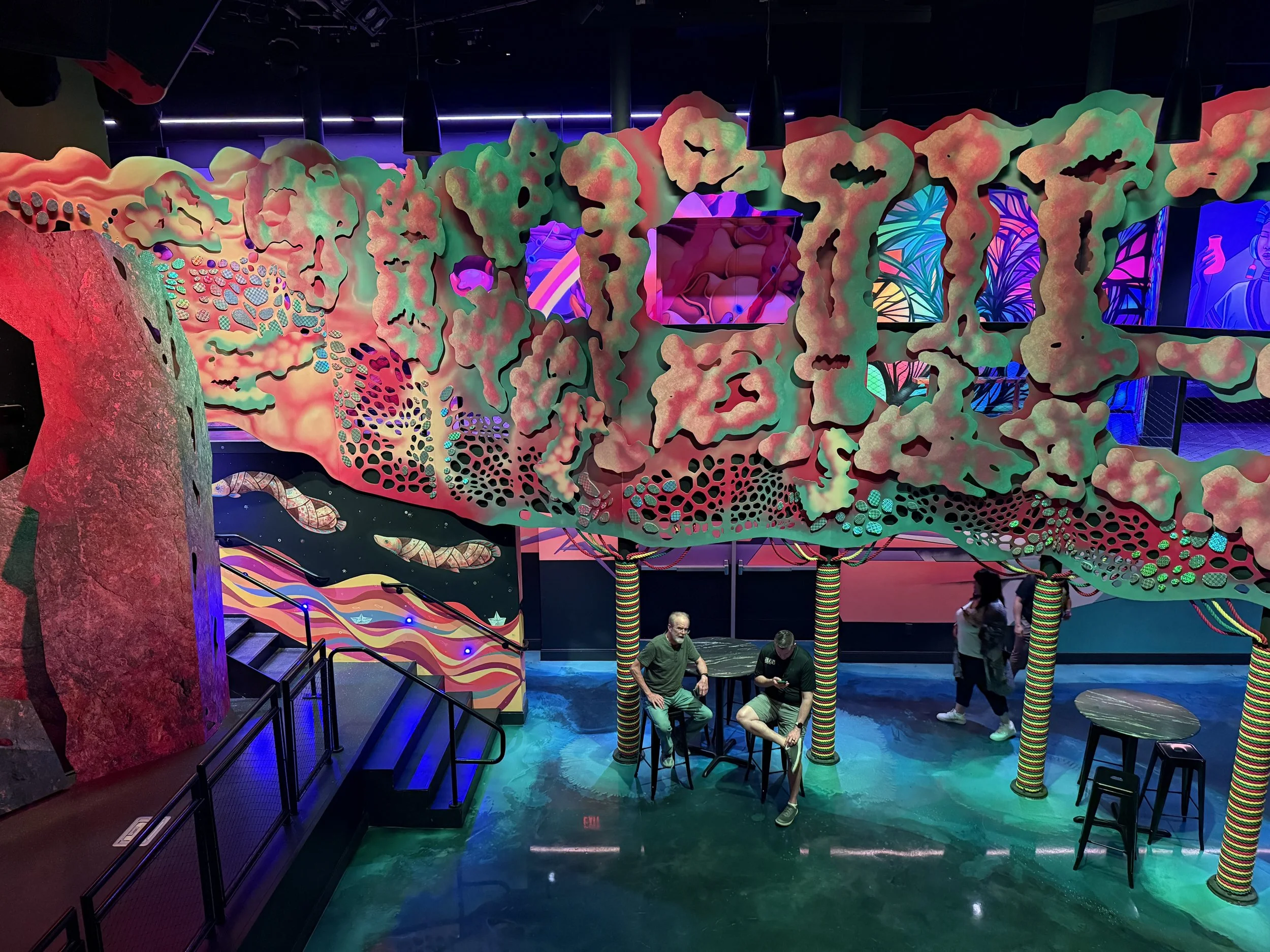 Looking down at a table and stool space with colorful murals at Meow Wolf Radio Tave in Houston, Texas
