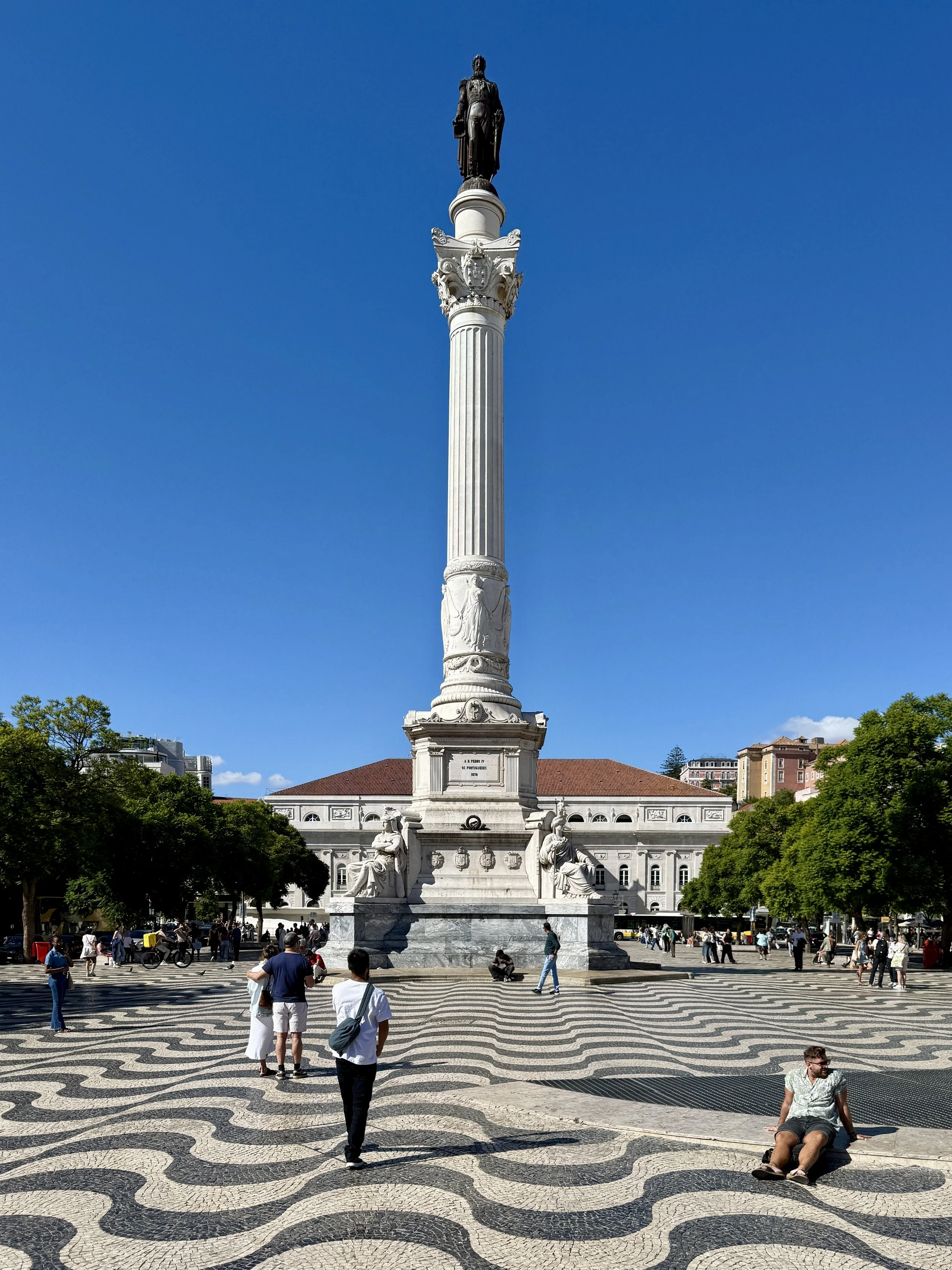 A tall column with a statue of Pedro IV in Rossio Square in Lisbon, Portugal, with undulating wavelike tiles on the ground