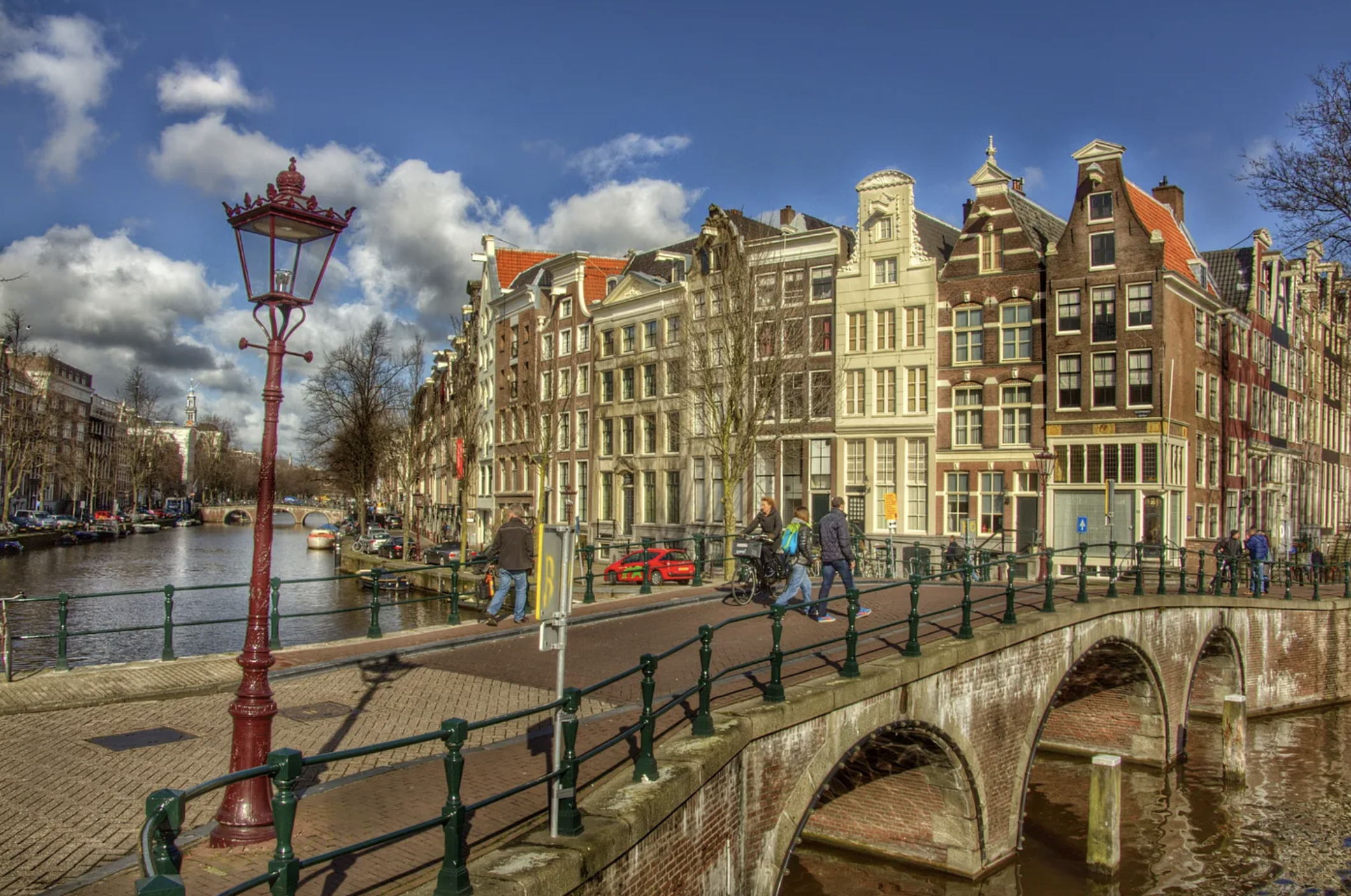 Tall narrow buildings up against each other in Amsterdam, with street lamp and people crossing a bridge