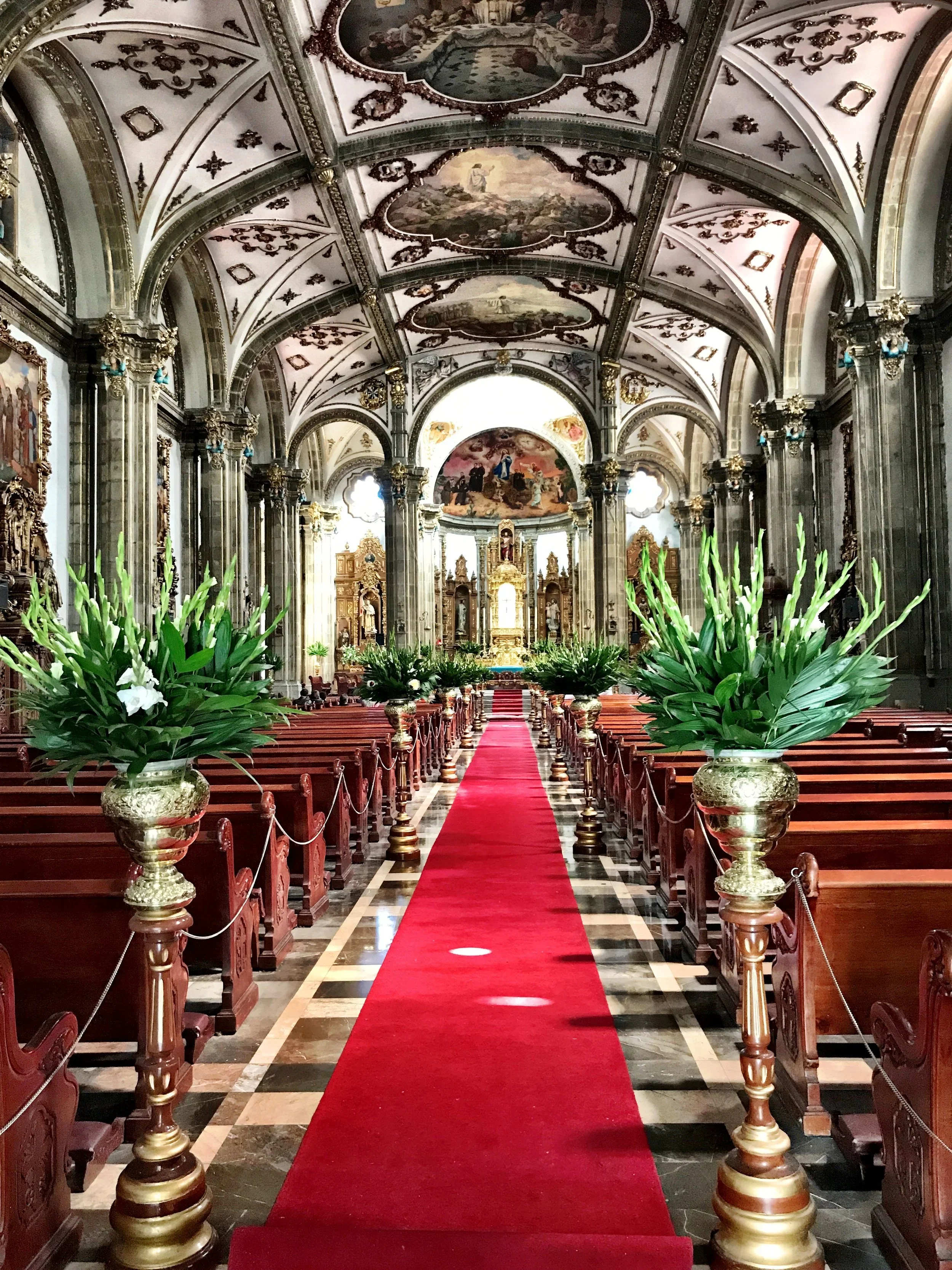 Murals on the ceiling, arches, pews and a red carpet runner inside Parroquia San Juan Bautista in Mexico City