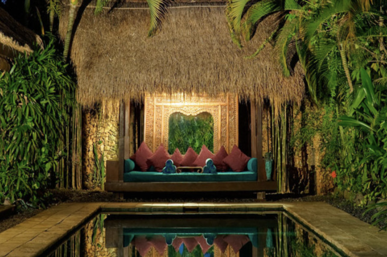 Beautiful seating area under thatched roof with ornate woodwork and sofa by pool at night on Bali