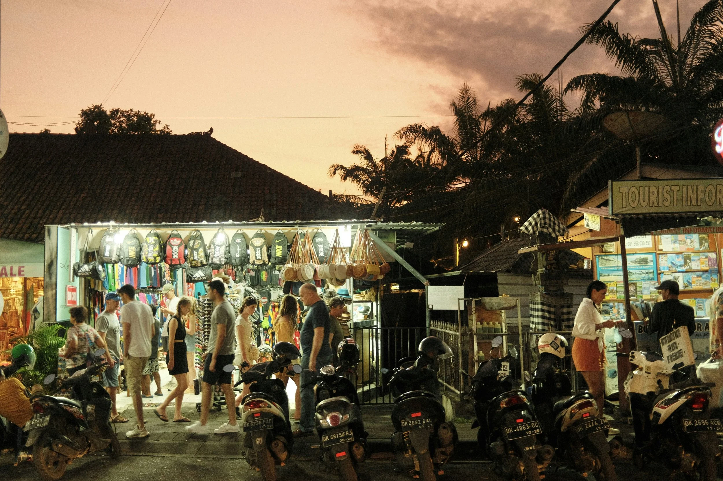 Night market in Bali near tourist information stand, a line of motorbikes and palm trees