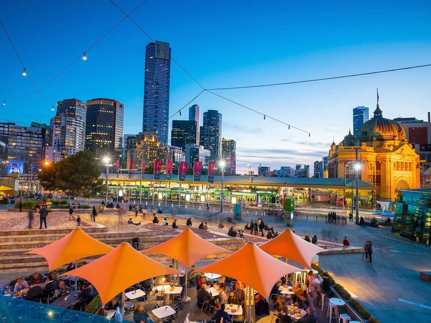 Diners eat under umbrellas by a station in Southbank, South Melbourne, Australia