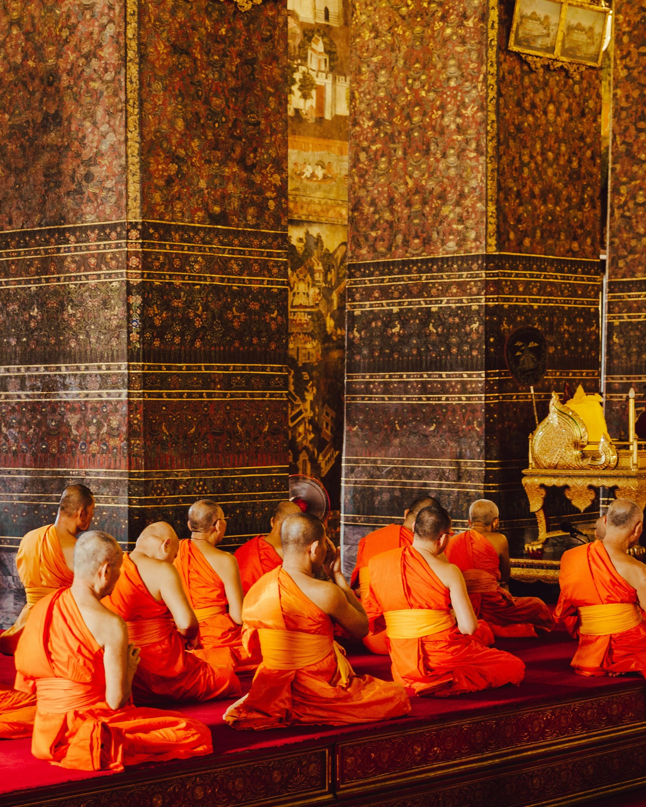 Buddhist monks in saffron robes sit and pray in a temple