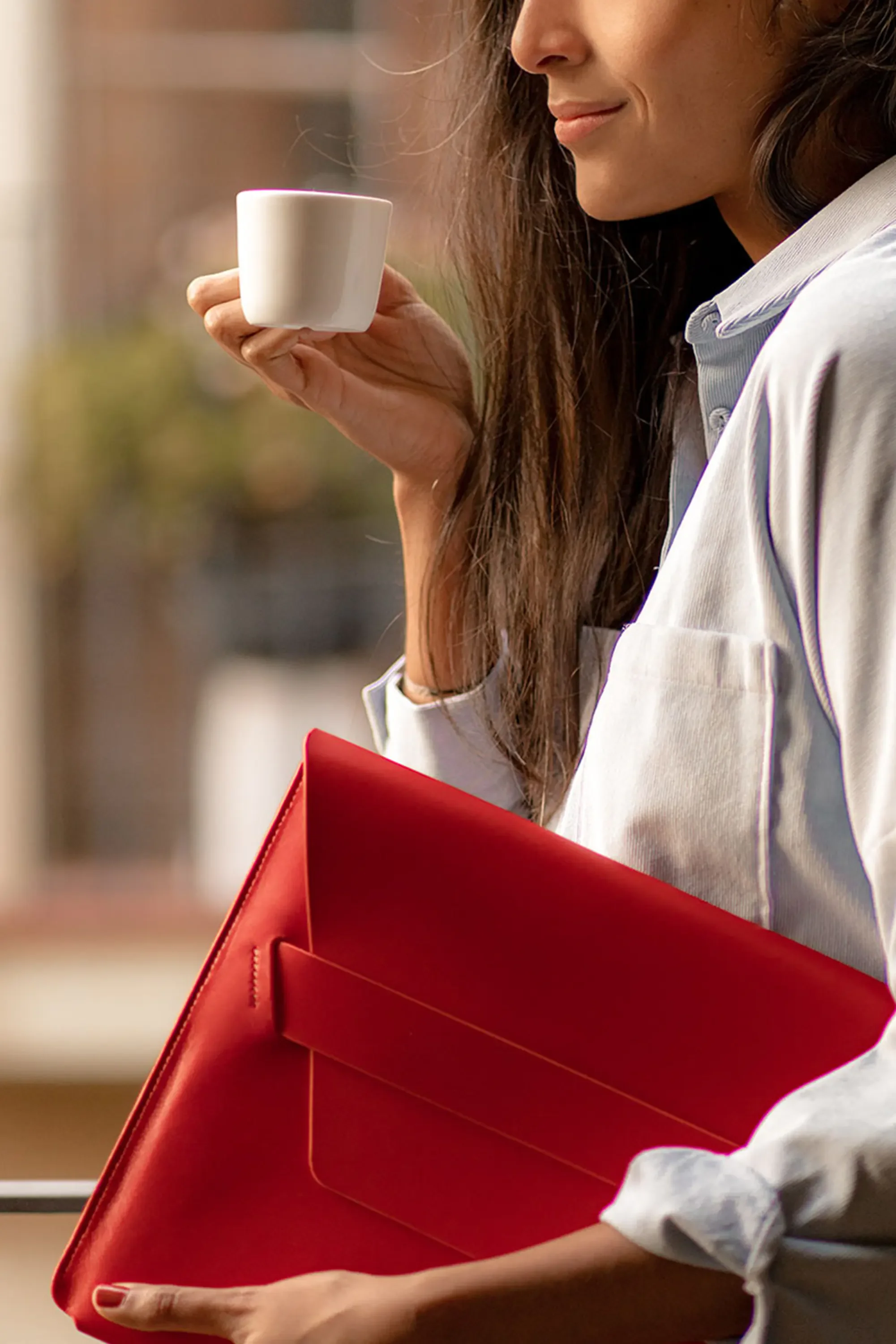 A woman holds an espresso cup and a red leather laptop case