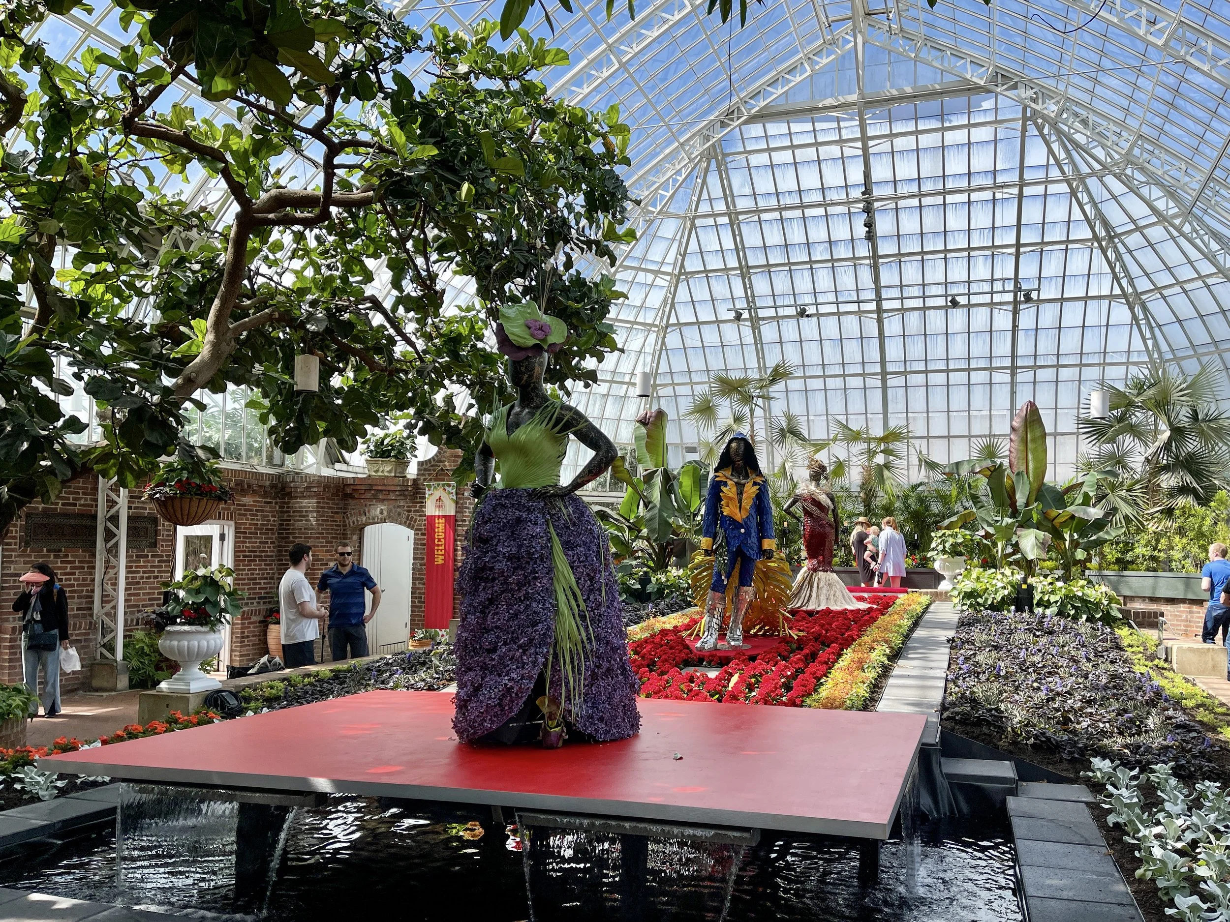 Mannequins with dresses made of plants on runway made of flowers in large conservatory at the Phipps