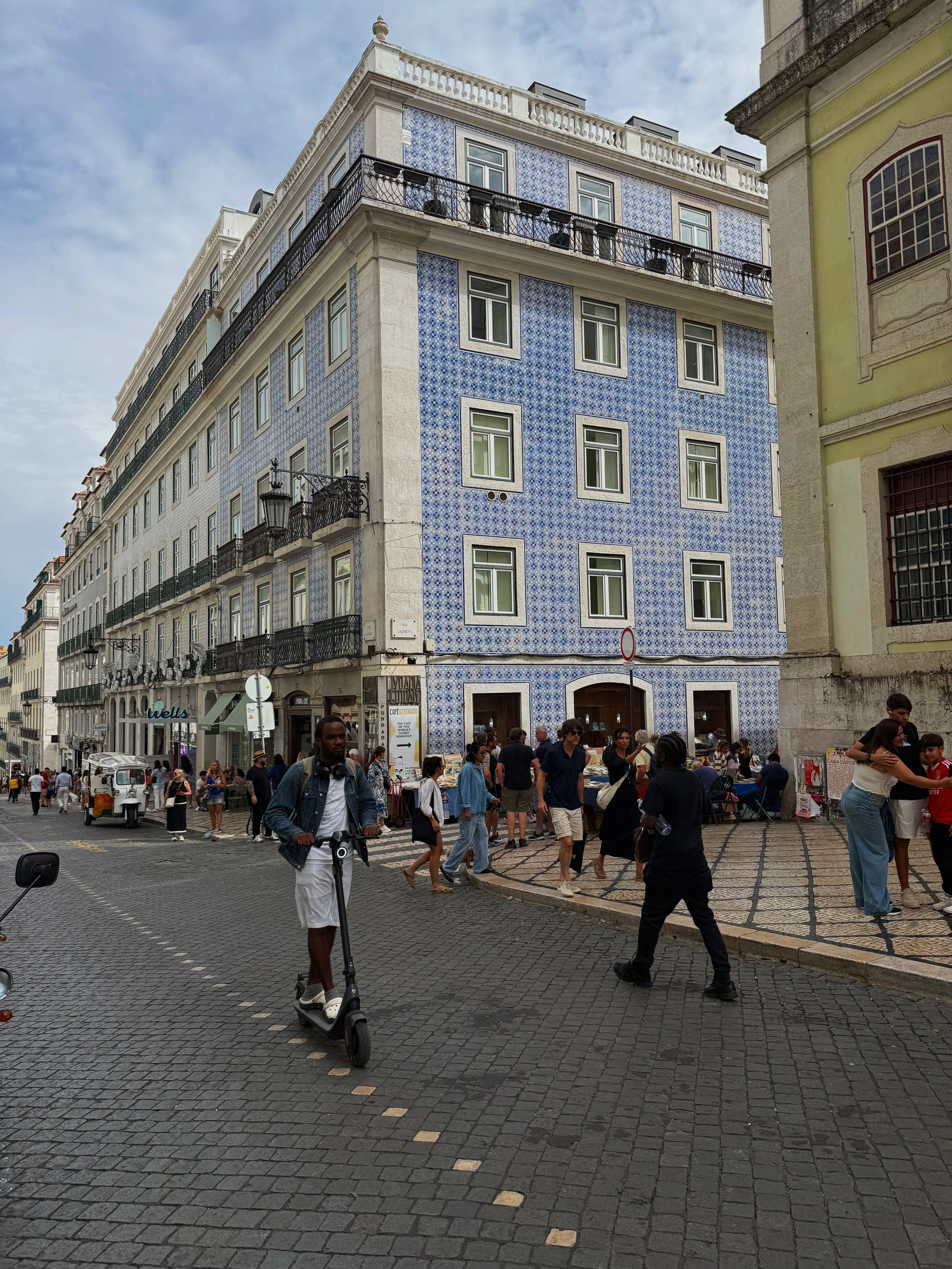 Pedestrians and a man on a scooter pass by a blue-tiled building in the Chiado neighborhood of Lisbon, Portugal