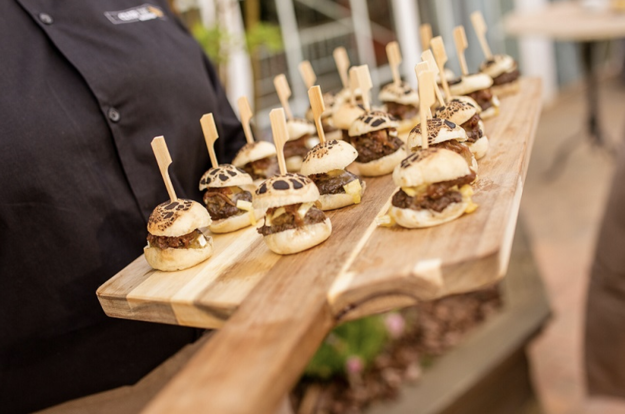 A server in black carries a wooden board with a bunch of pintxos of sliders