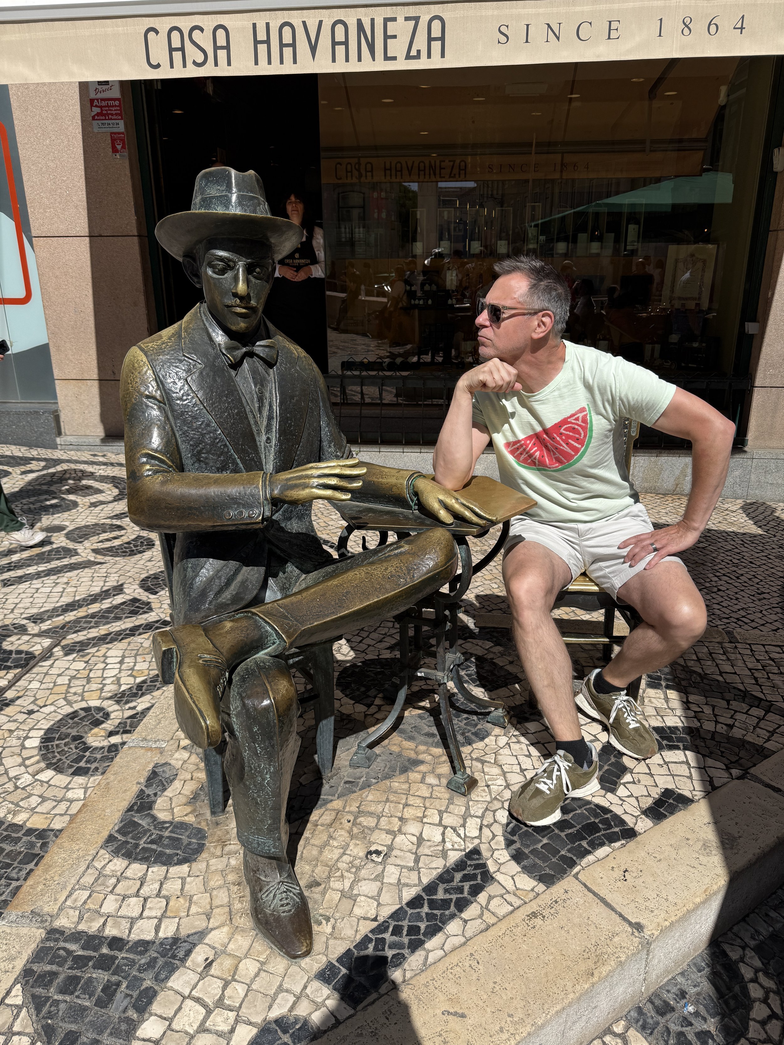 A statue of the famous poet Fernando Pessoa with a man inspecting him in the Chiado district in Lisbon, Portugal