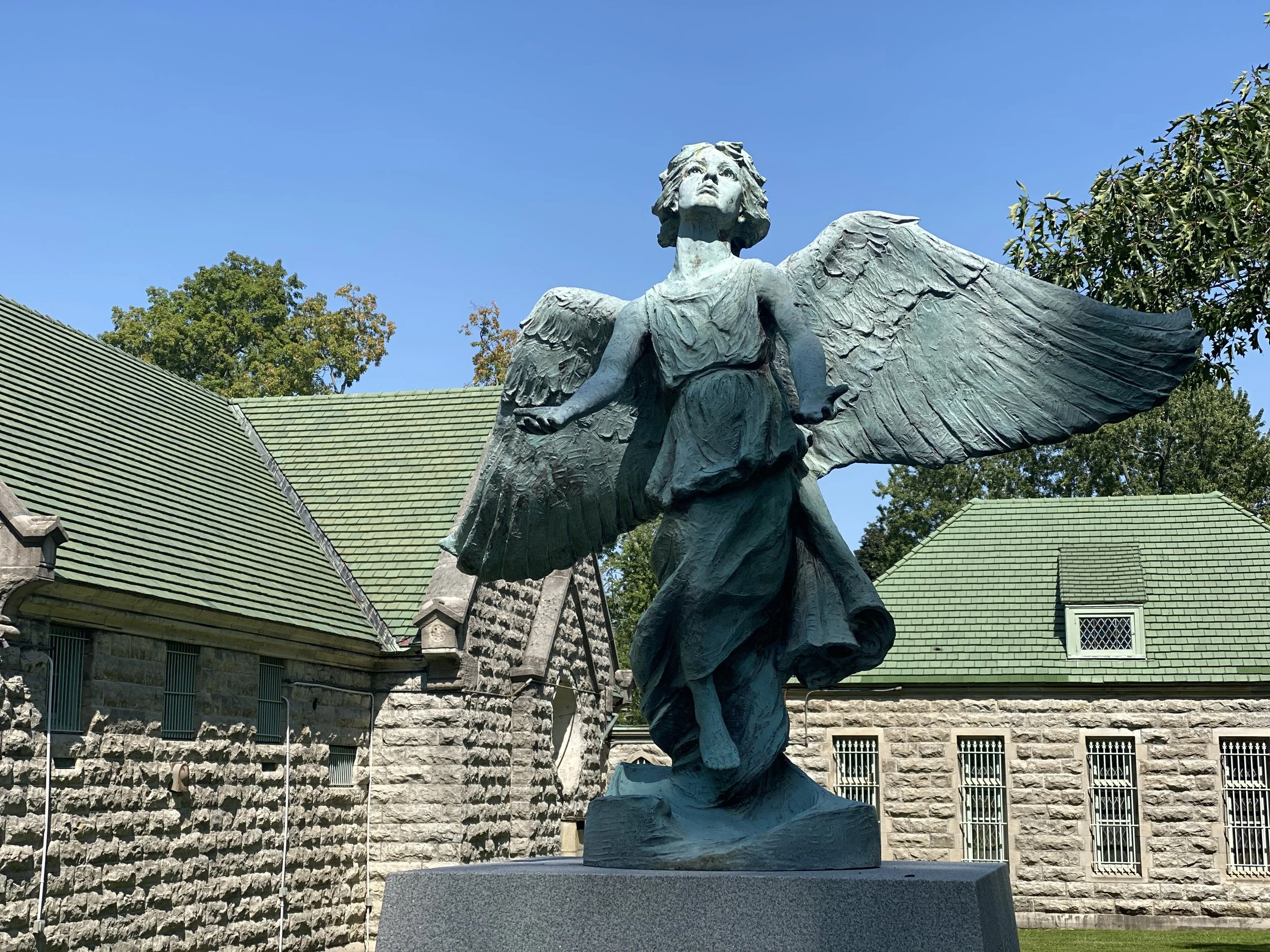 Bronze statue of angel by stone chapel on the grounds of Forest Lawn Cemetery