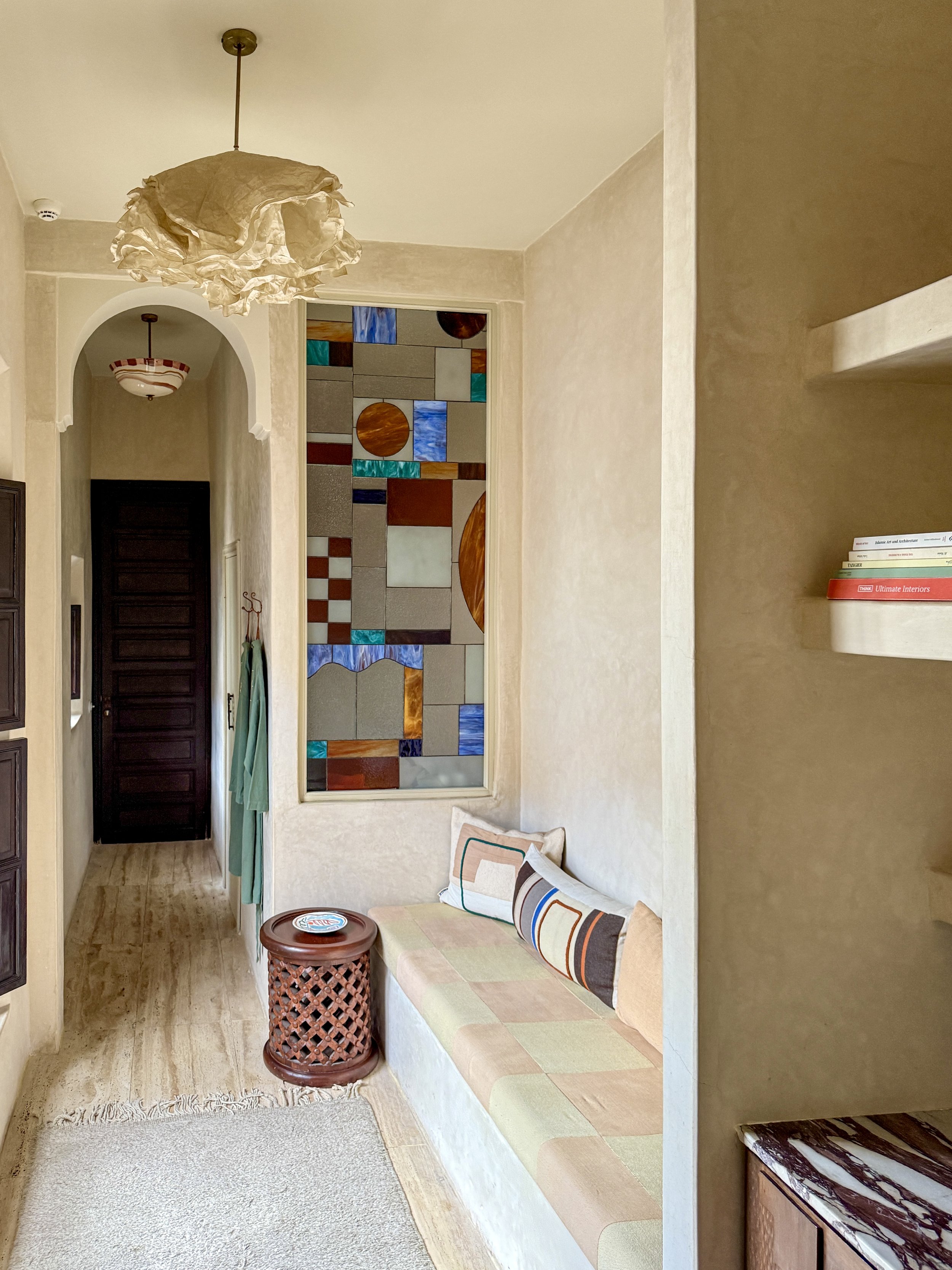 Stained glass window, seating nook and narrow arch with hanging lamps in the Cocoon suite at Rosemary Riad in Marrakech