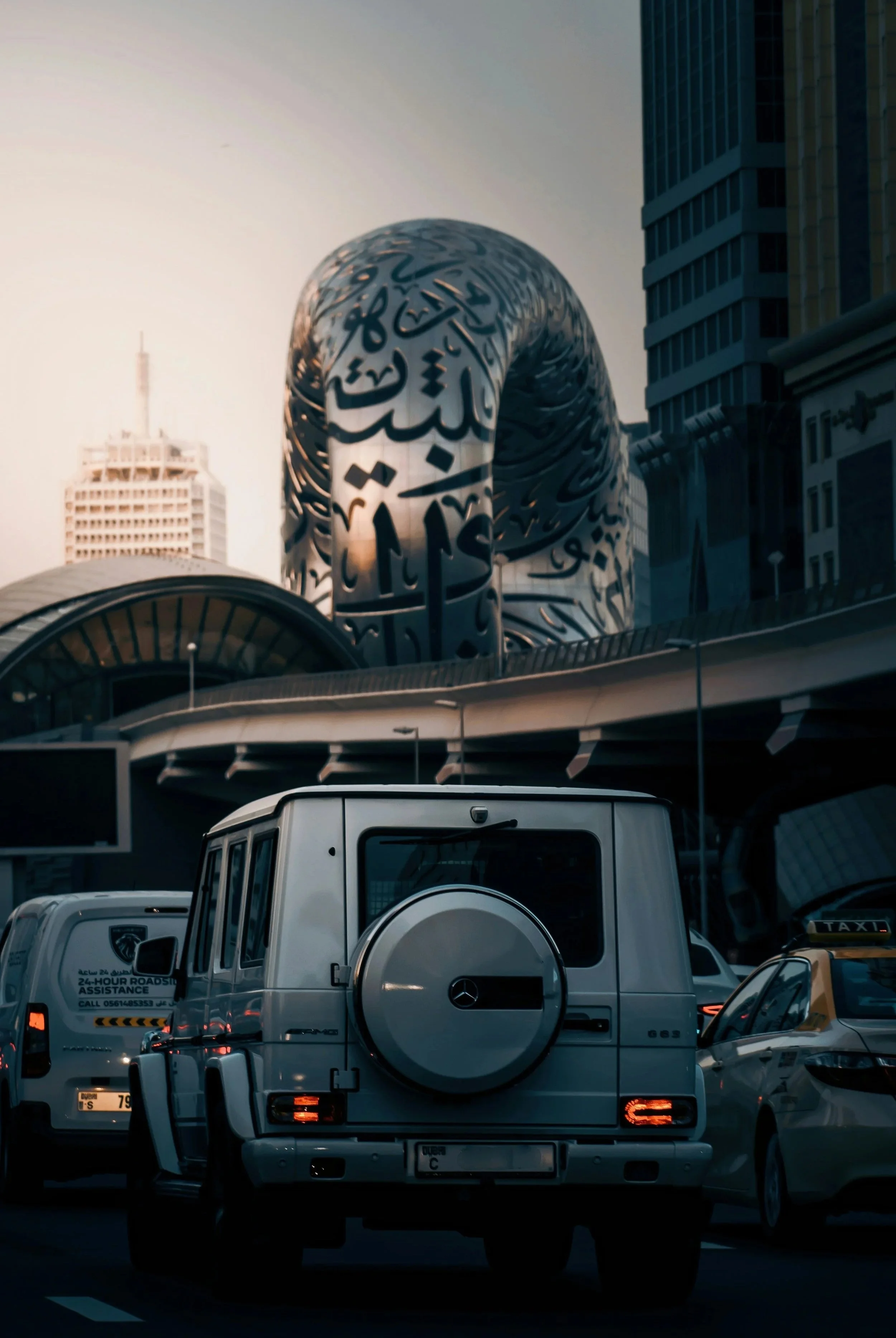 The back of a jeep and other vehicles passing by the Arabic-covered ring of the Dubai Museum of the Future