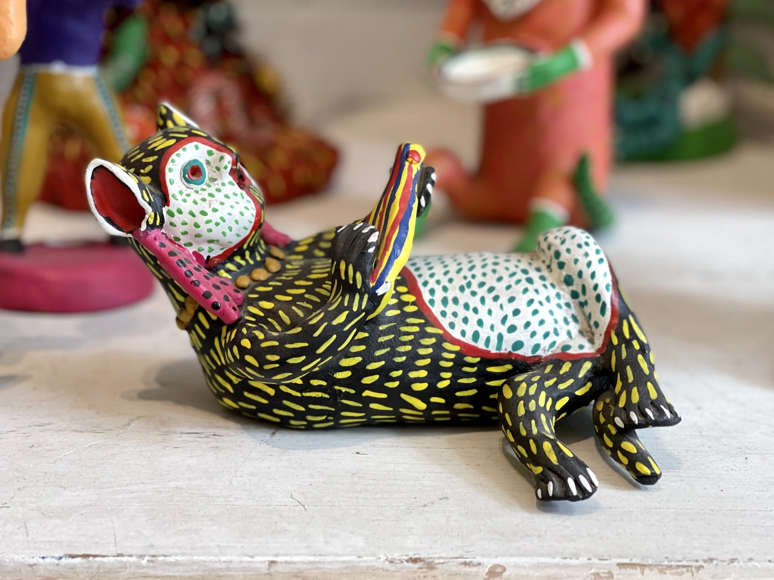 Alebrije of a lounging lemur-like creature with black body with yellow accents and white and blue stomach