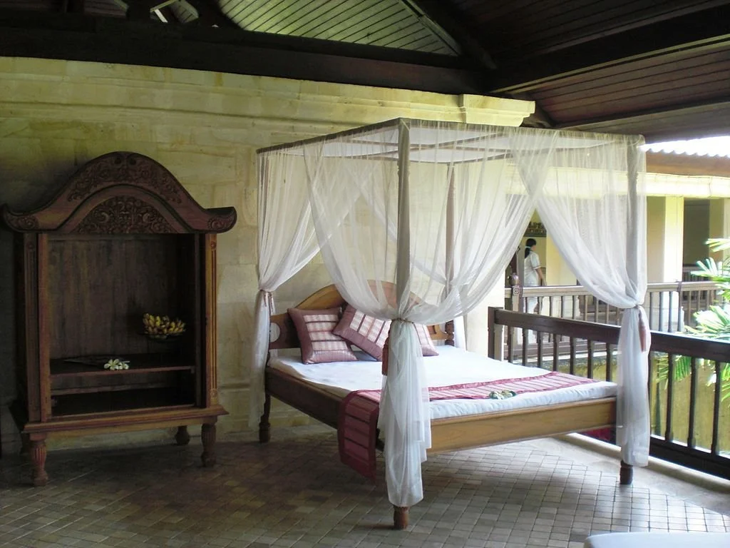 Bed with mosquito netting next to armoire and railing by open-air courtyard at hotel in Bali