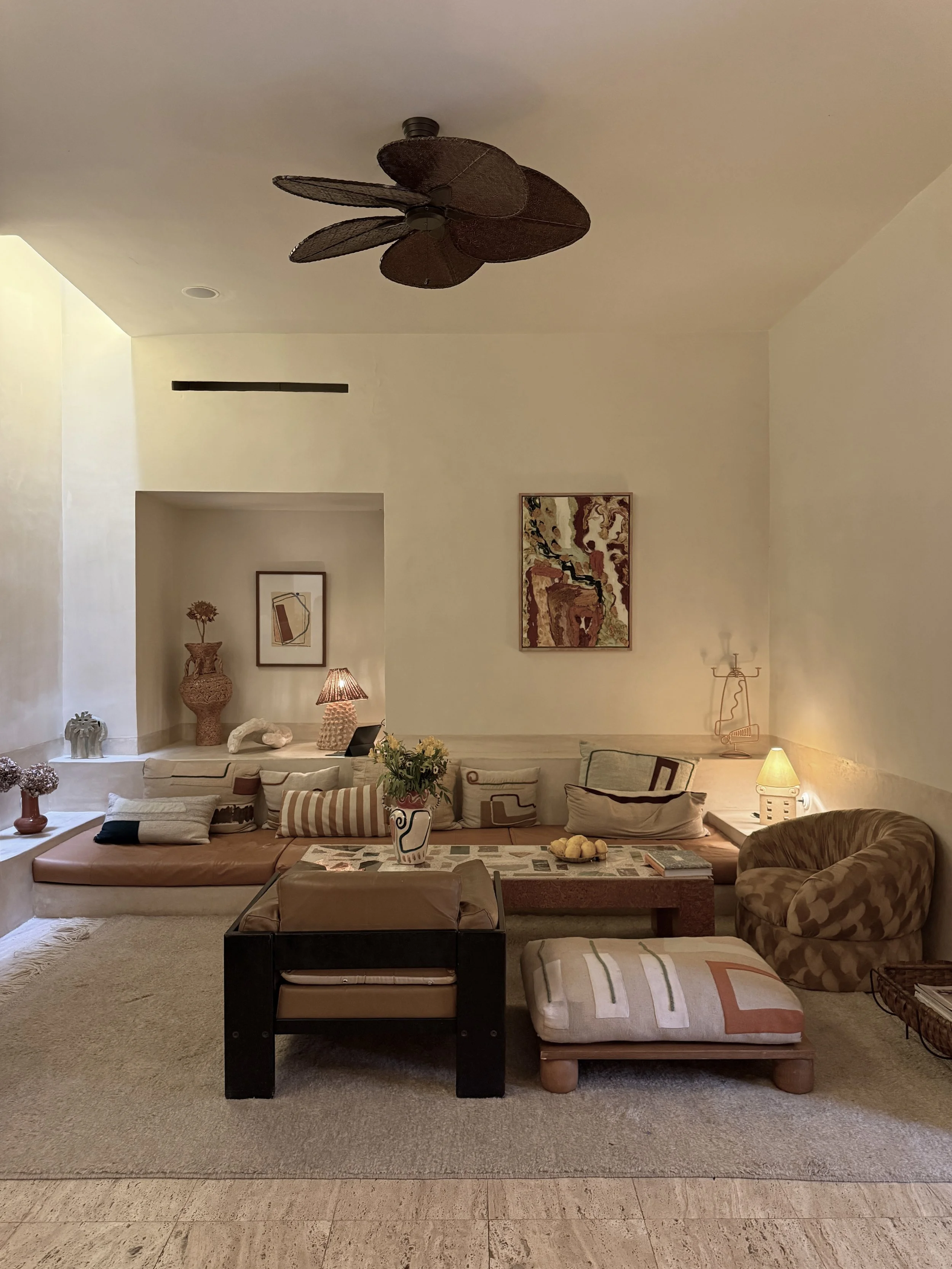The living room at Riad Rosemary in Marrakech with built-in banquette, vintage furniture and tiered shelves lined with art books, ceramics and objects by LRNCE