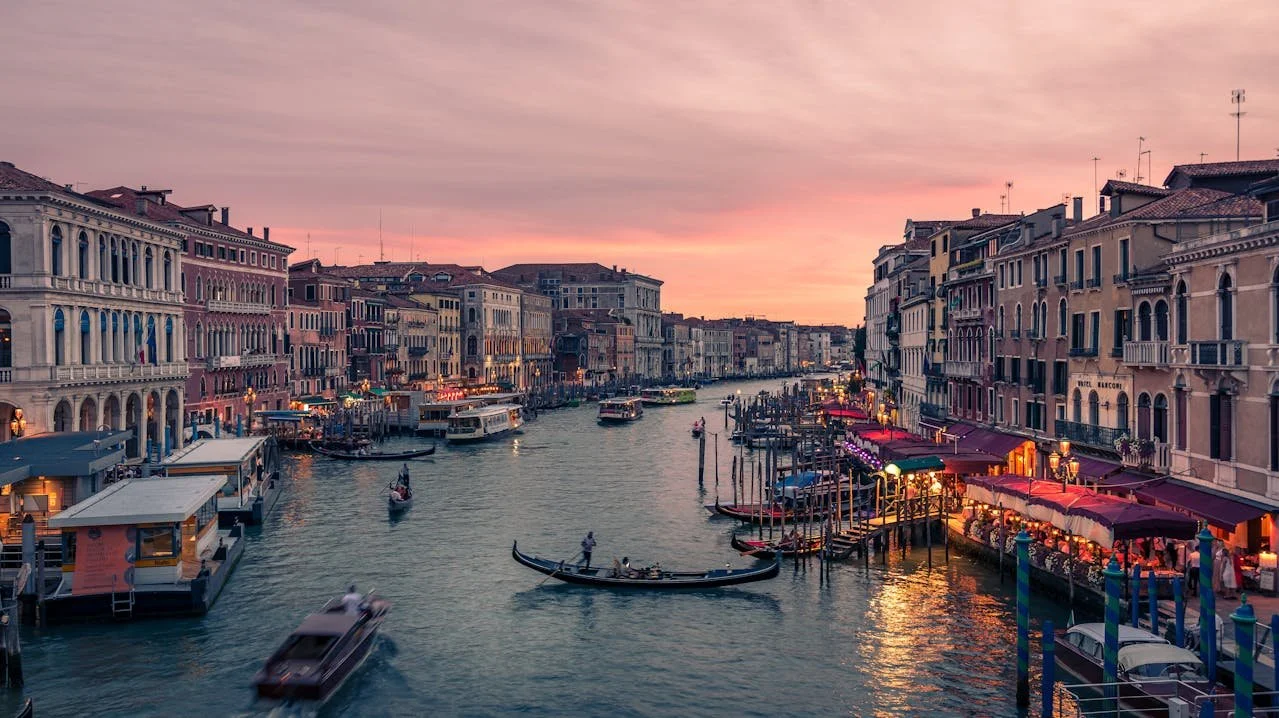 View of Venice at sunset, with buildings lining the canal, filled with gondolas and other boats